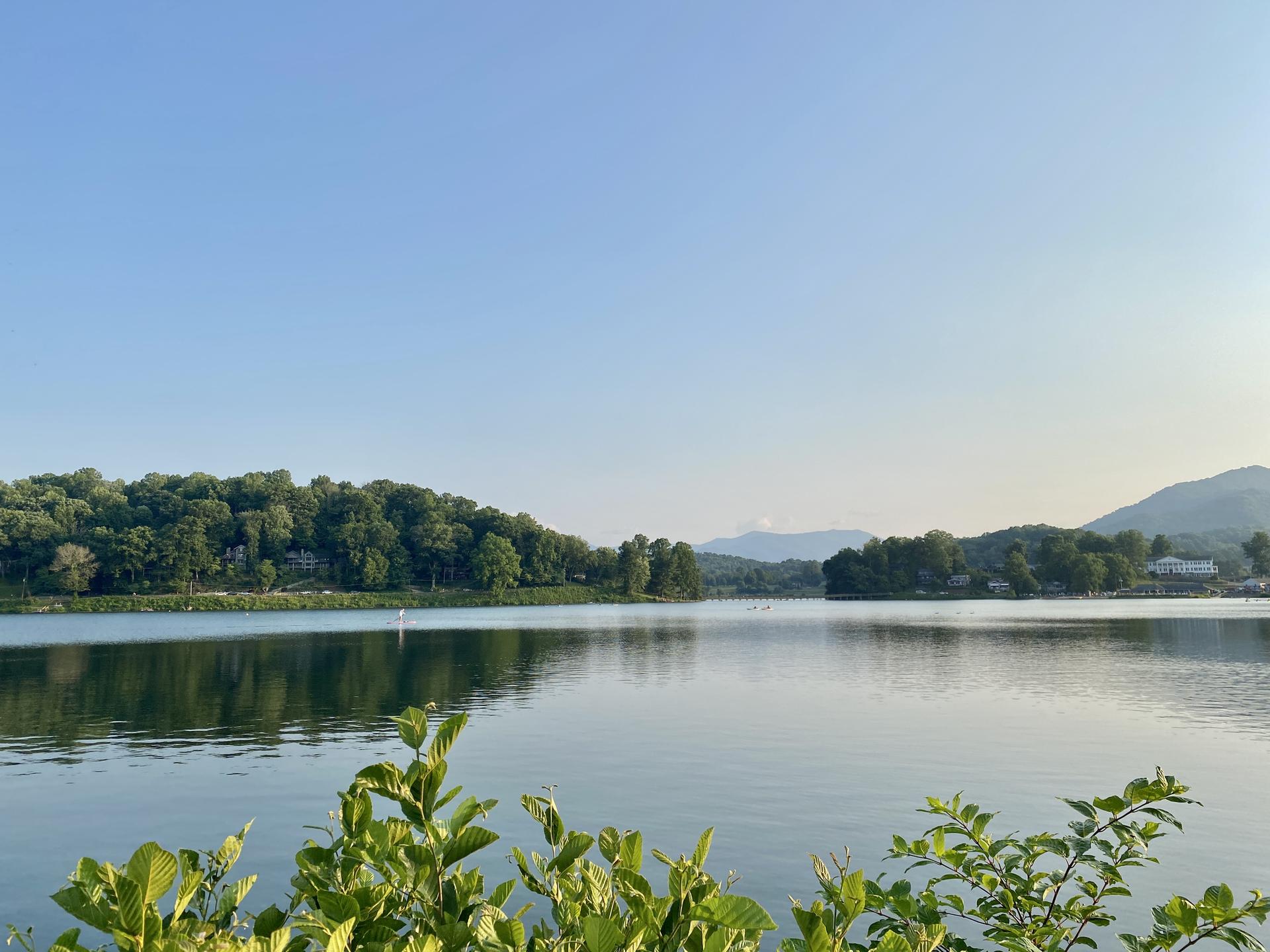 Serene lake surrounded by green hills under a clear blue sky.