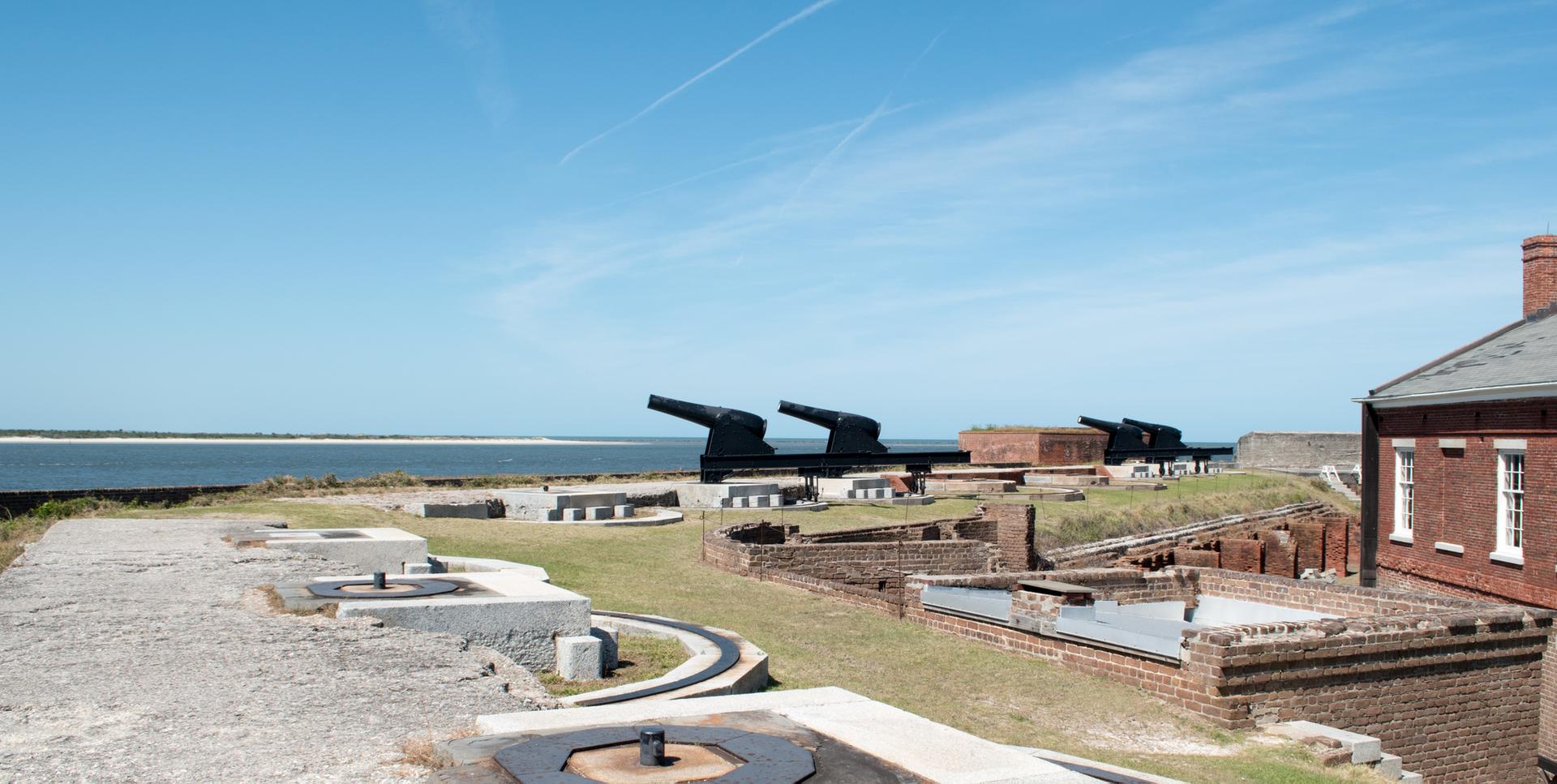 Historic fort with large cannons overlooking water under a bright blue sky.