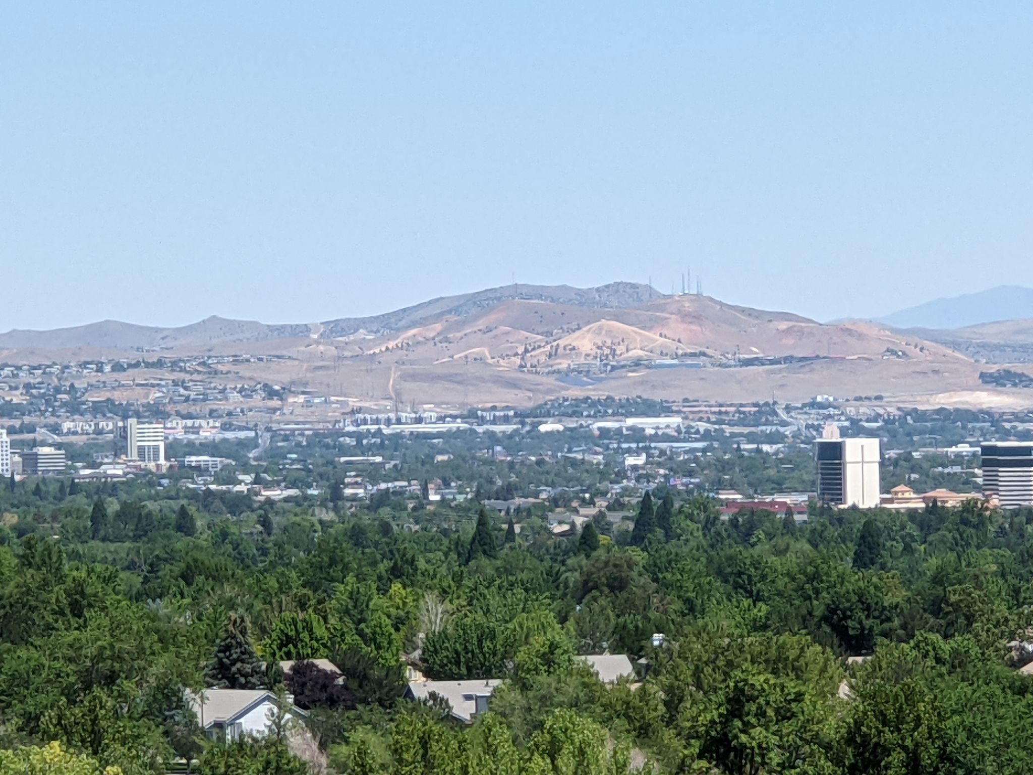 Expansive view of a city with lush trees, buildings, and arid mountains under a clear sky. - Bartley Ranch to Crystal Peak Park loop
