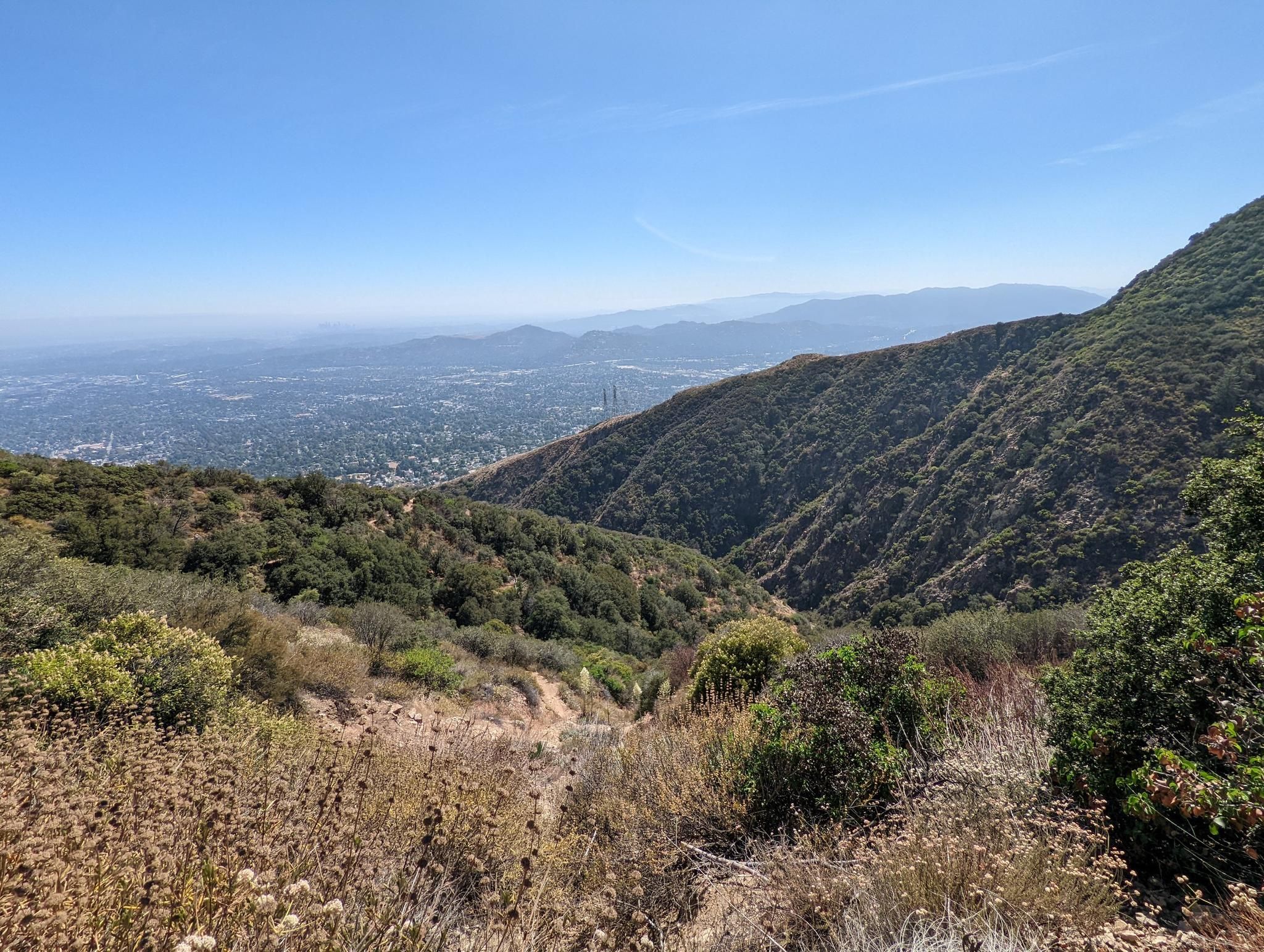 Expansive view of a green mountain valley and distant city under a clear sky. - Mount Lowe and Echo Mountain Loop