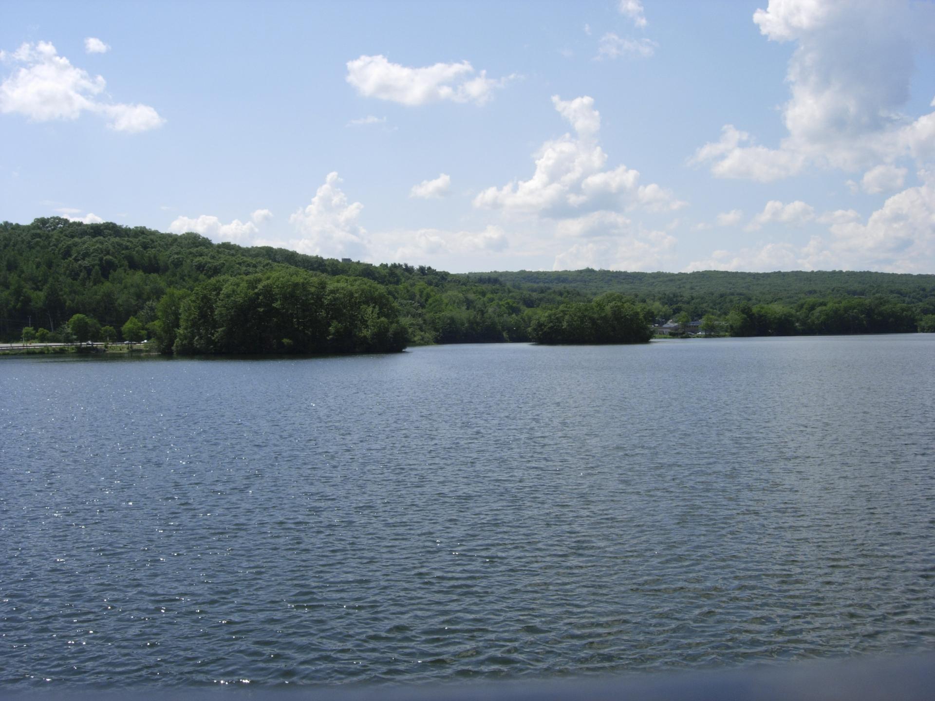 A wide lake with forested hills under a partly cloudy sky during daytime.