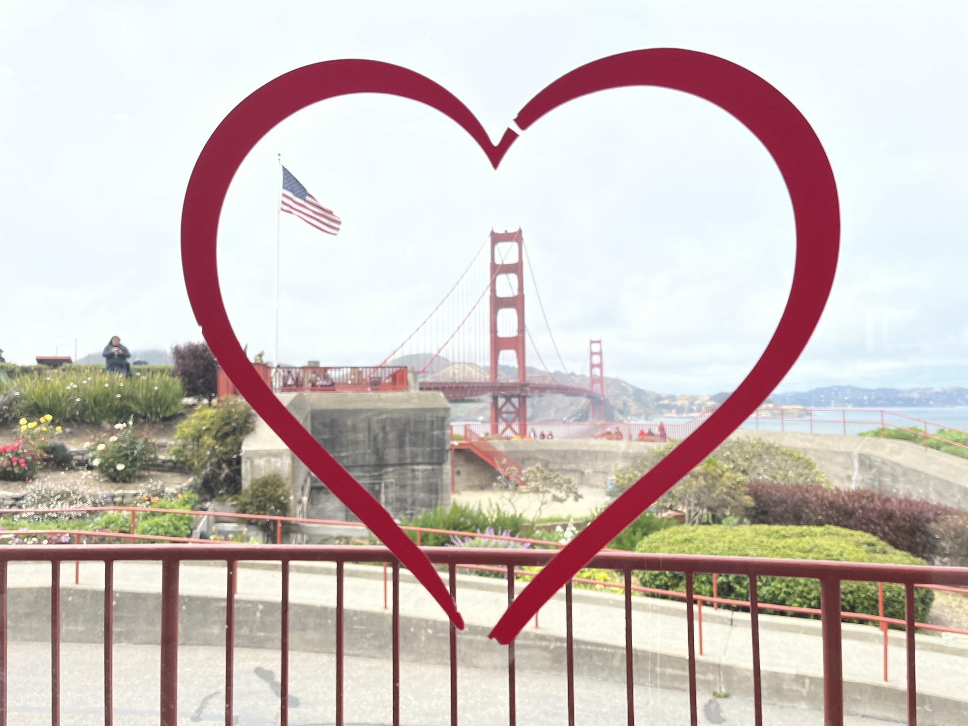 Red heart outline framing a distant red suspension bridge and flag.