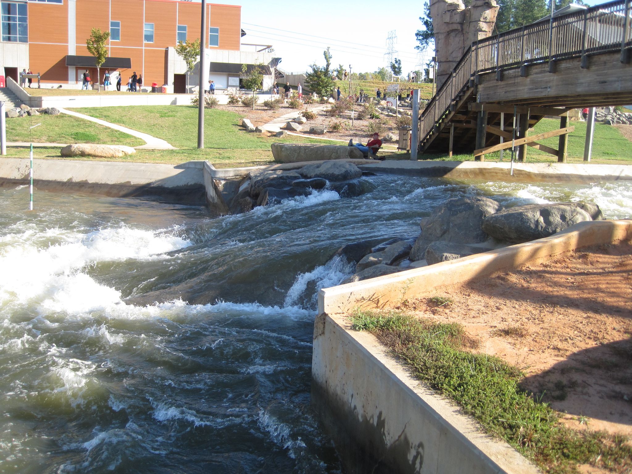 Rushing water in a man-made channel with a bridge and buildings under sun. - Panda Trail loop from Hawk Island