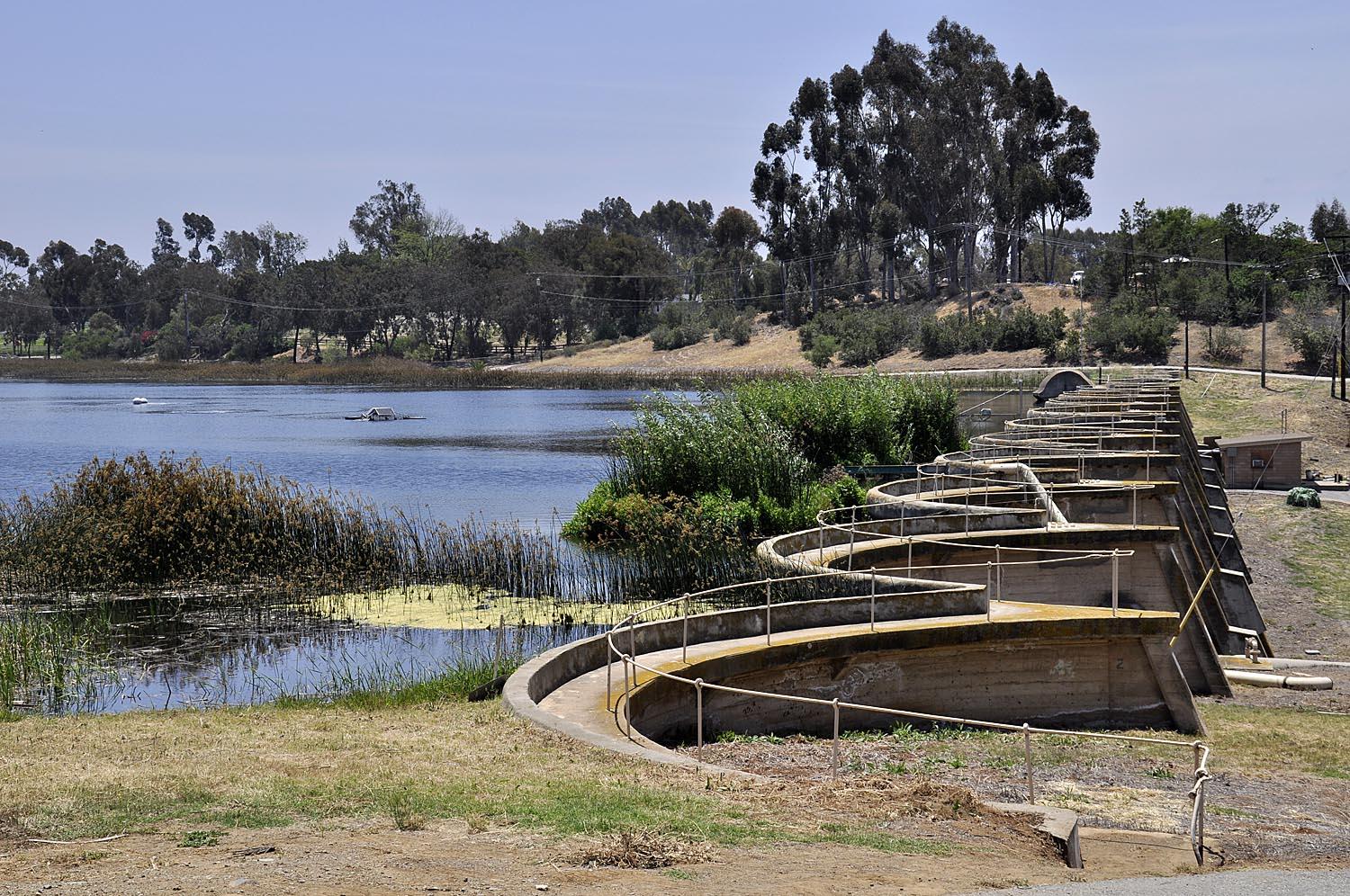 Sunny view of a lake with concrete structures and distant boats.