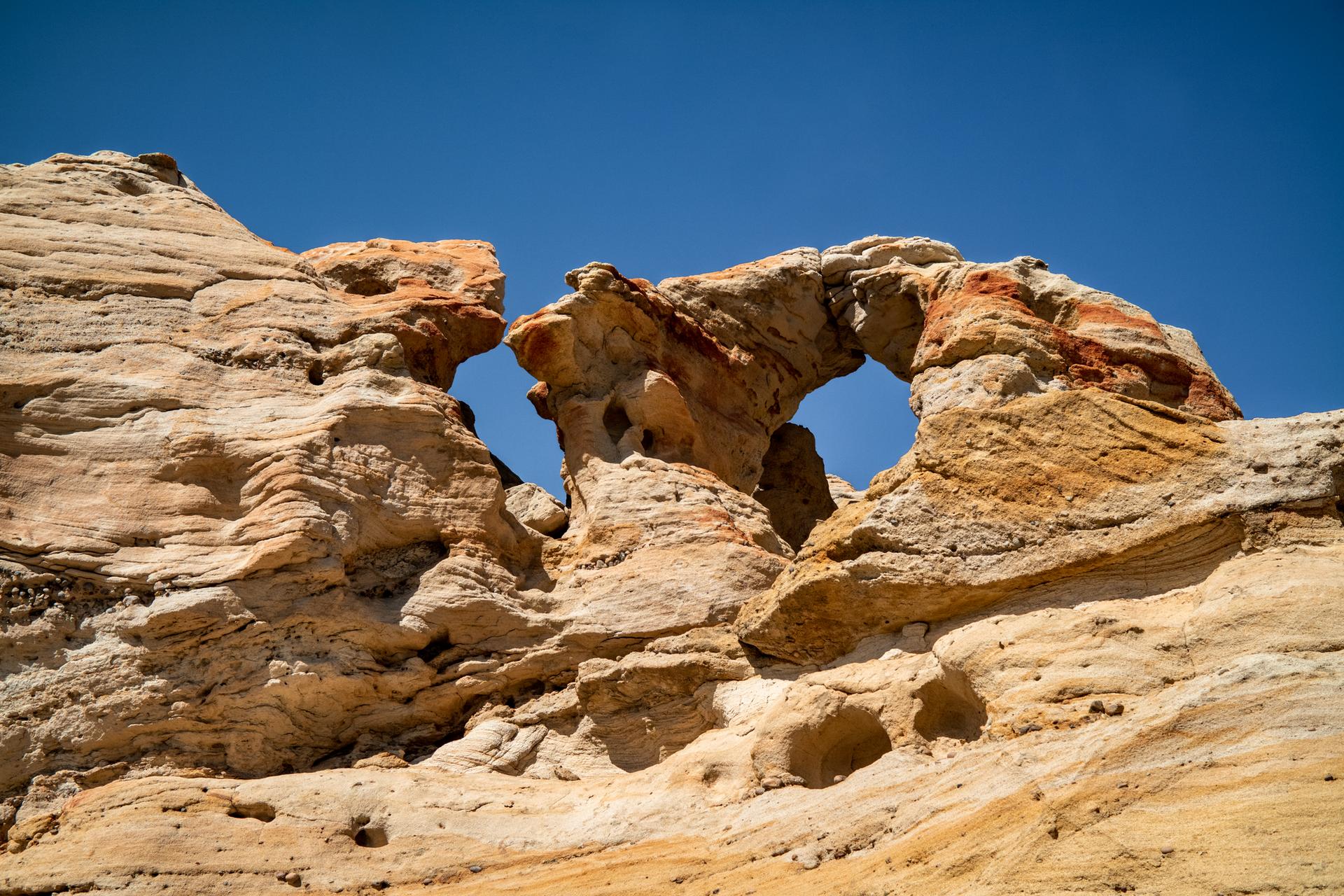 Natural rock arches and weathered formations in a desert under a blue sky.