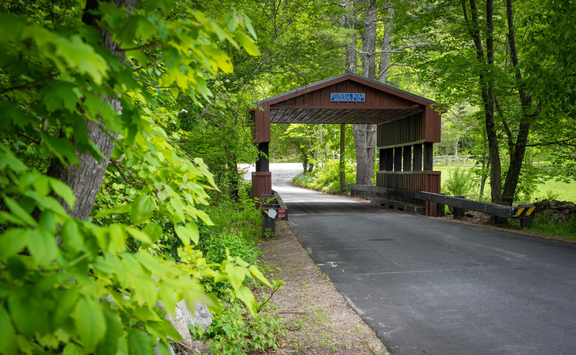 A wooden covered bridge over a road, surrounded by lush green trees.