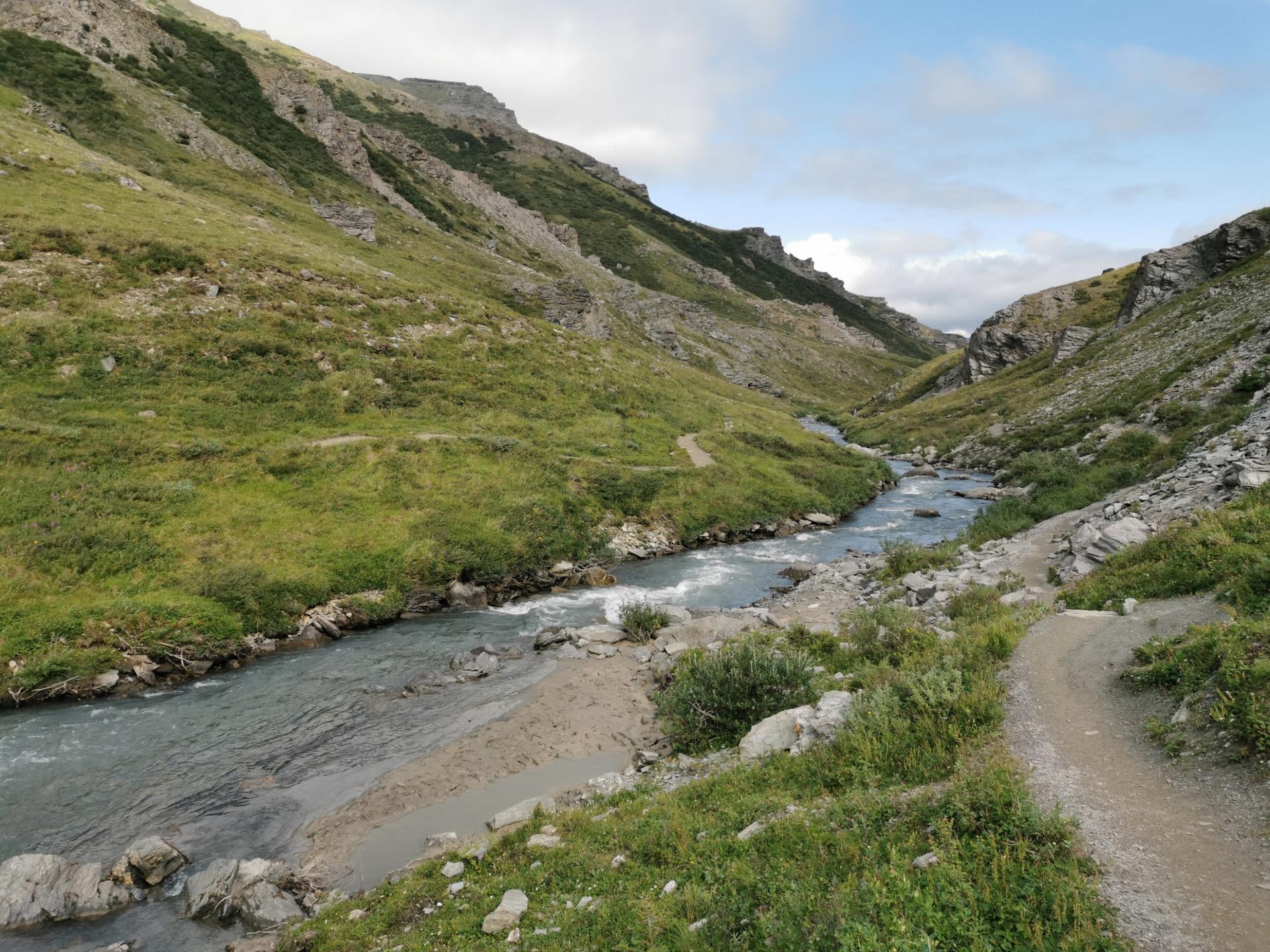 A winding river flows through a lush green mountain valley under cloudy skies.