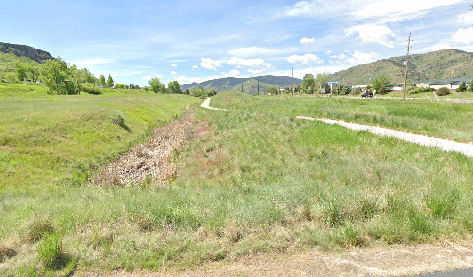 Sunny green valley with a dry ditch and a distant paved path.