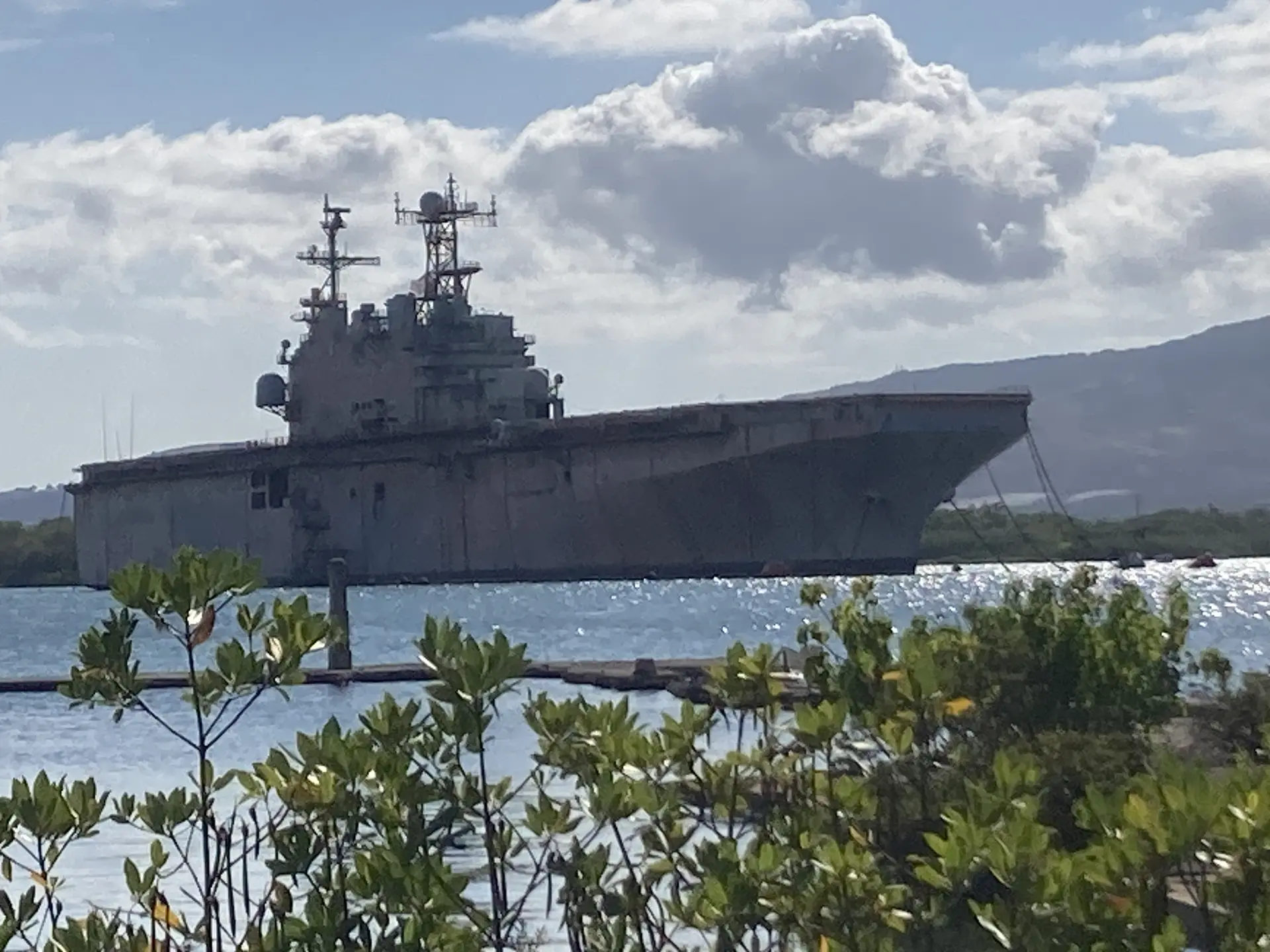 A large gray warship floats on sparkling water under a partly cloudy sky.