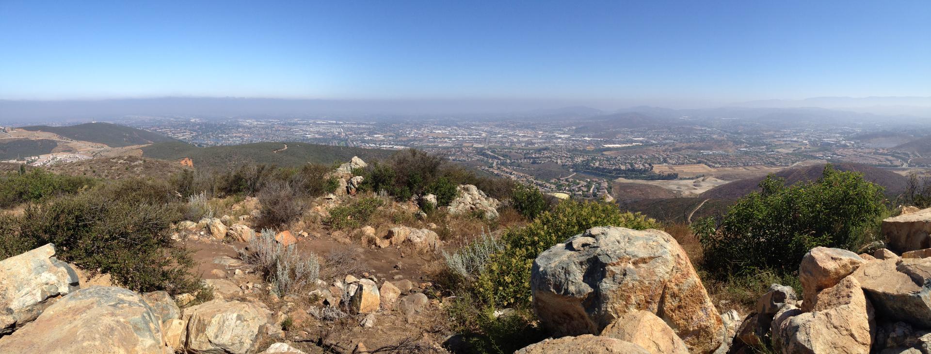 Panoramic view from a rocky hill overlooking a hazy city on a clear day.
