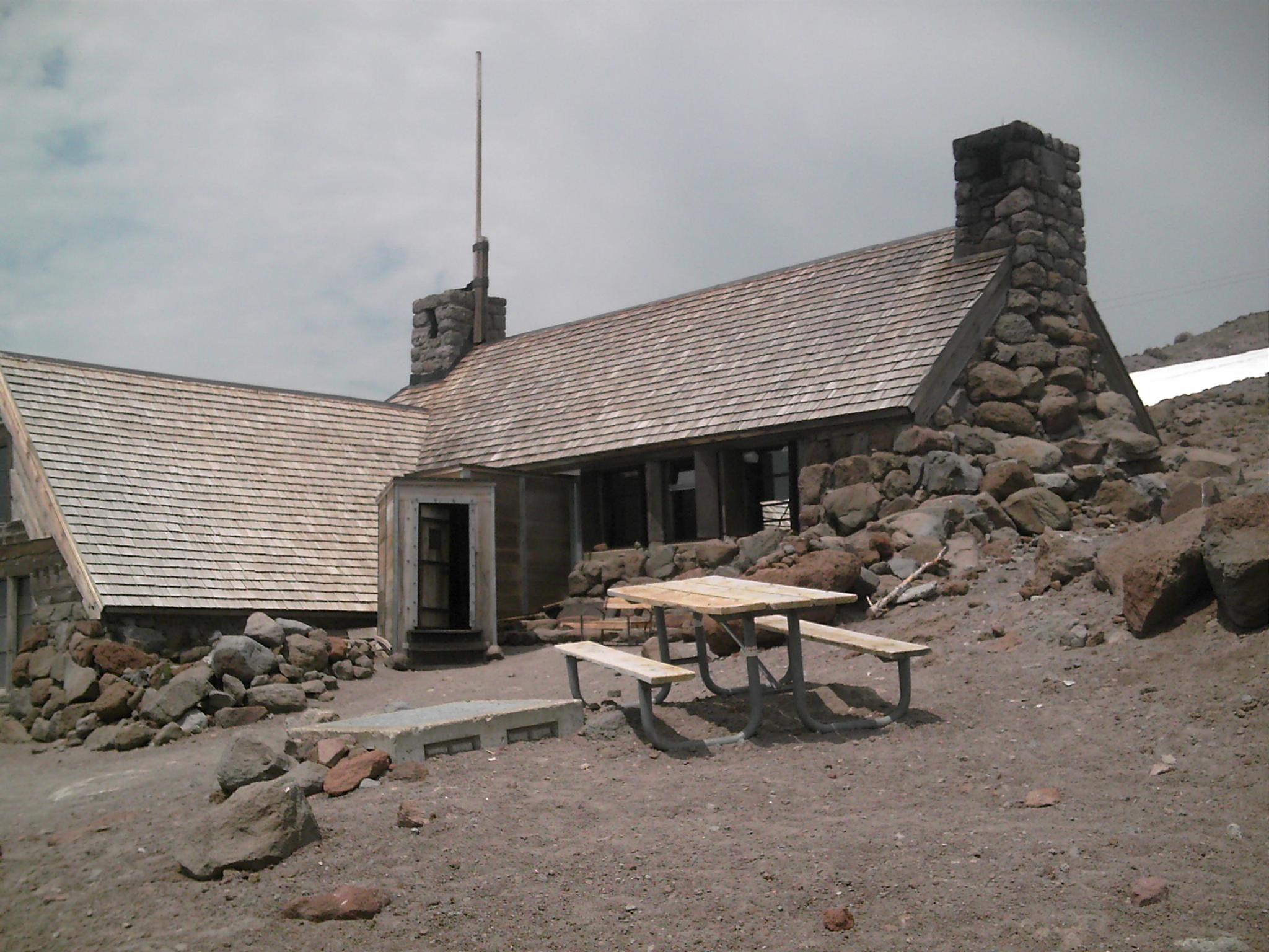 Rustic stone and wood building with a shingled roof on rocky terrain.