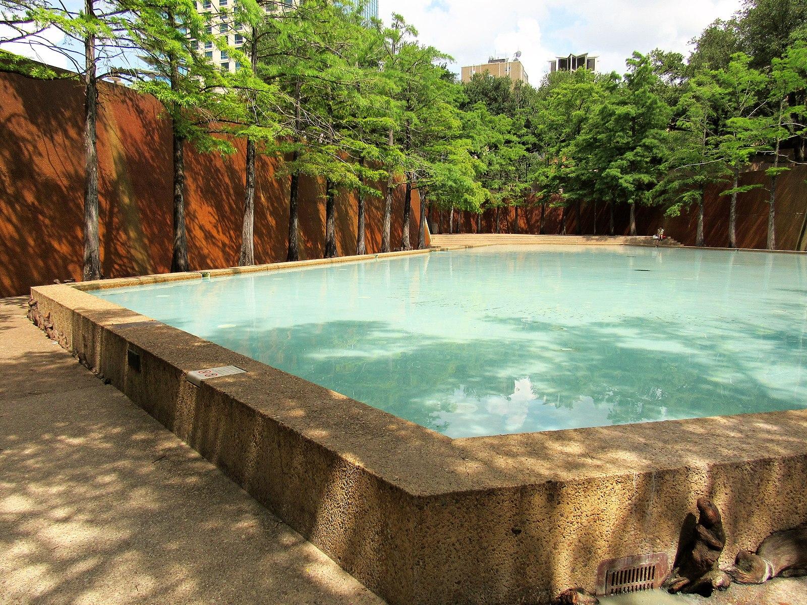 Rectangular pool with clear water, surrounded by trees and concrete walls.