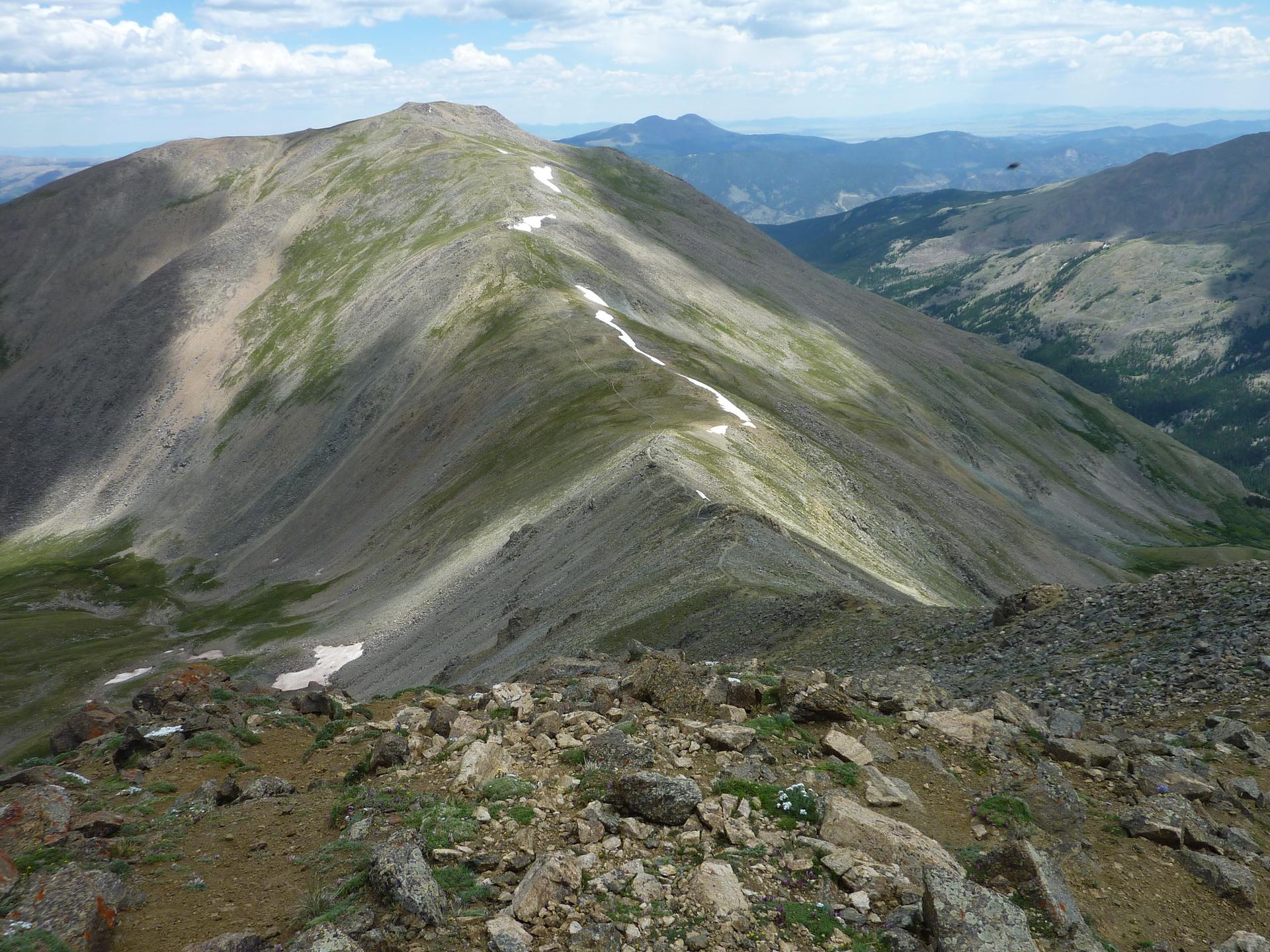 Panoramic view of a long mountain ridge with rocky foreground under cloudy sky.