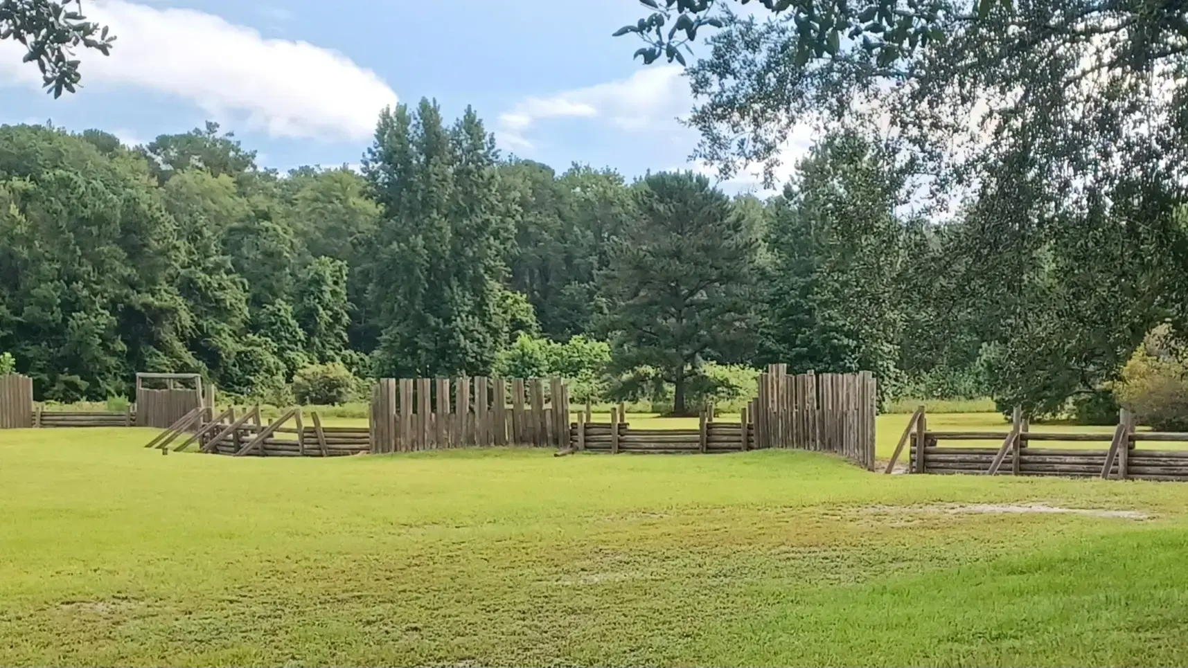 Wooden fences in a wide green field backed by dense forest.