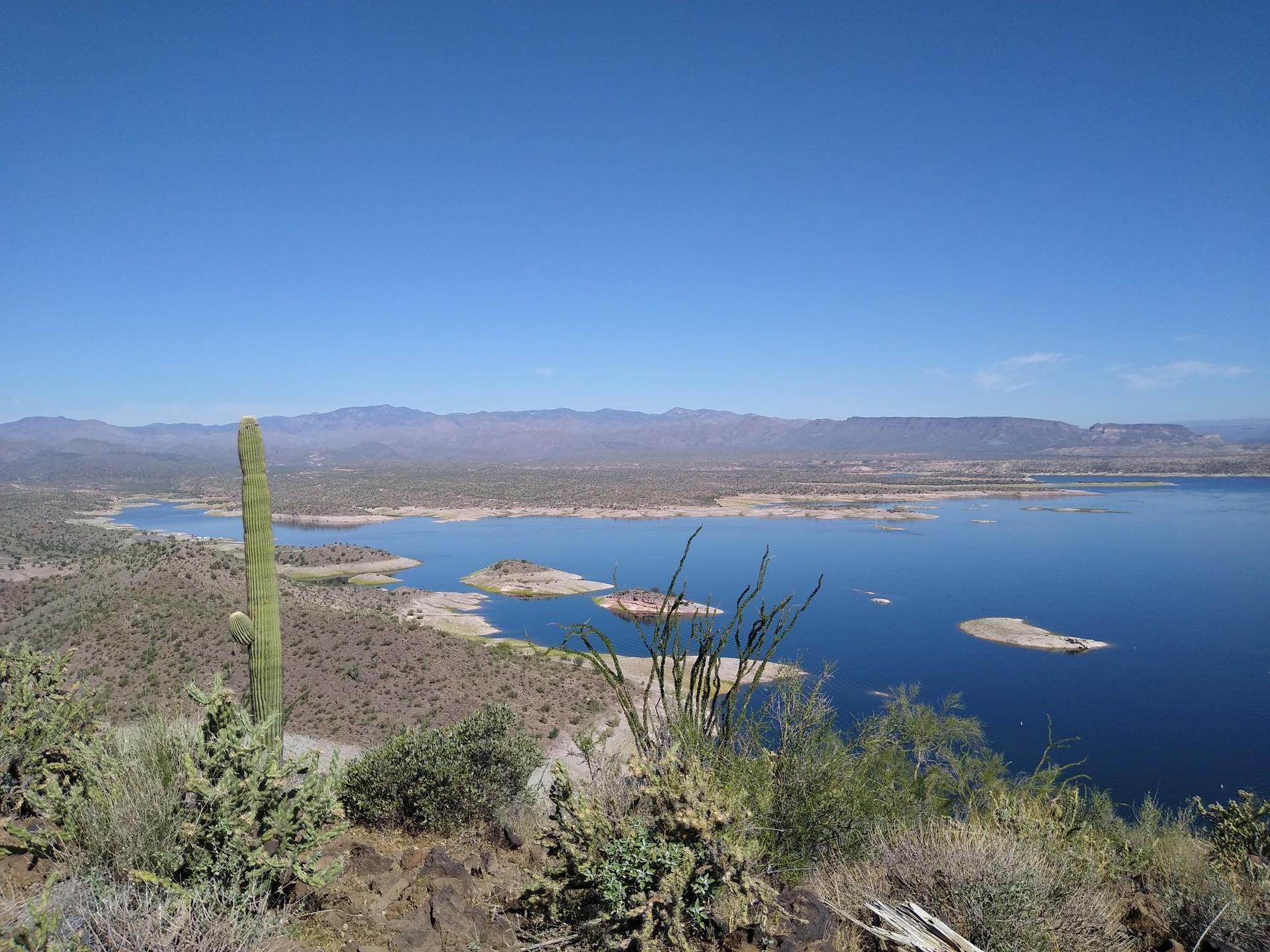 Wide desert landscape with a large lake and distant mountains under clear sky.