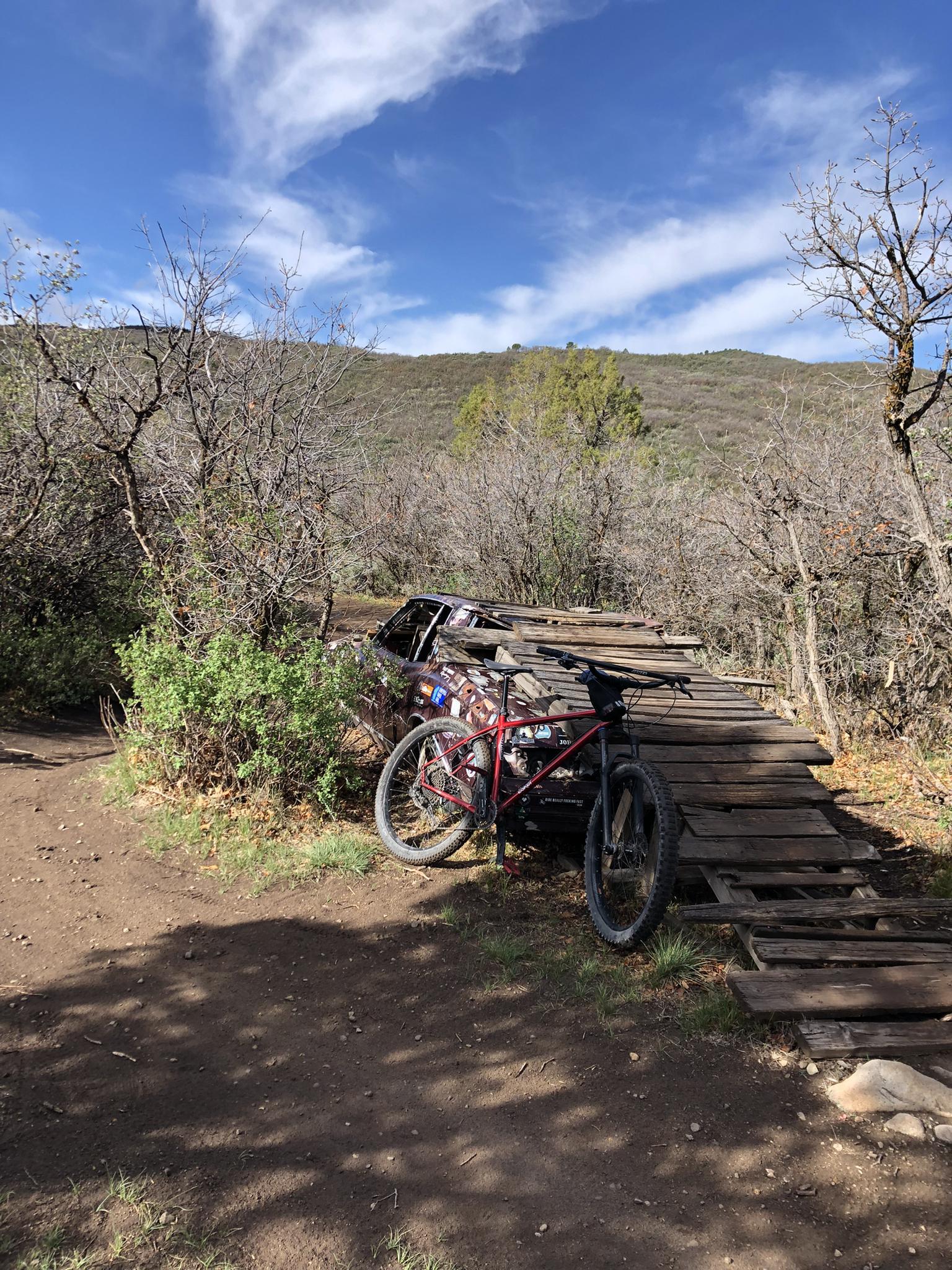 Mountain bike next to a wooden ramp on a sunny, dry hillside.