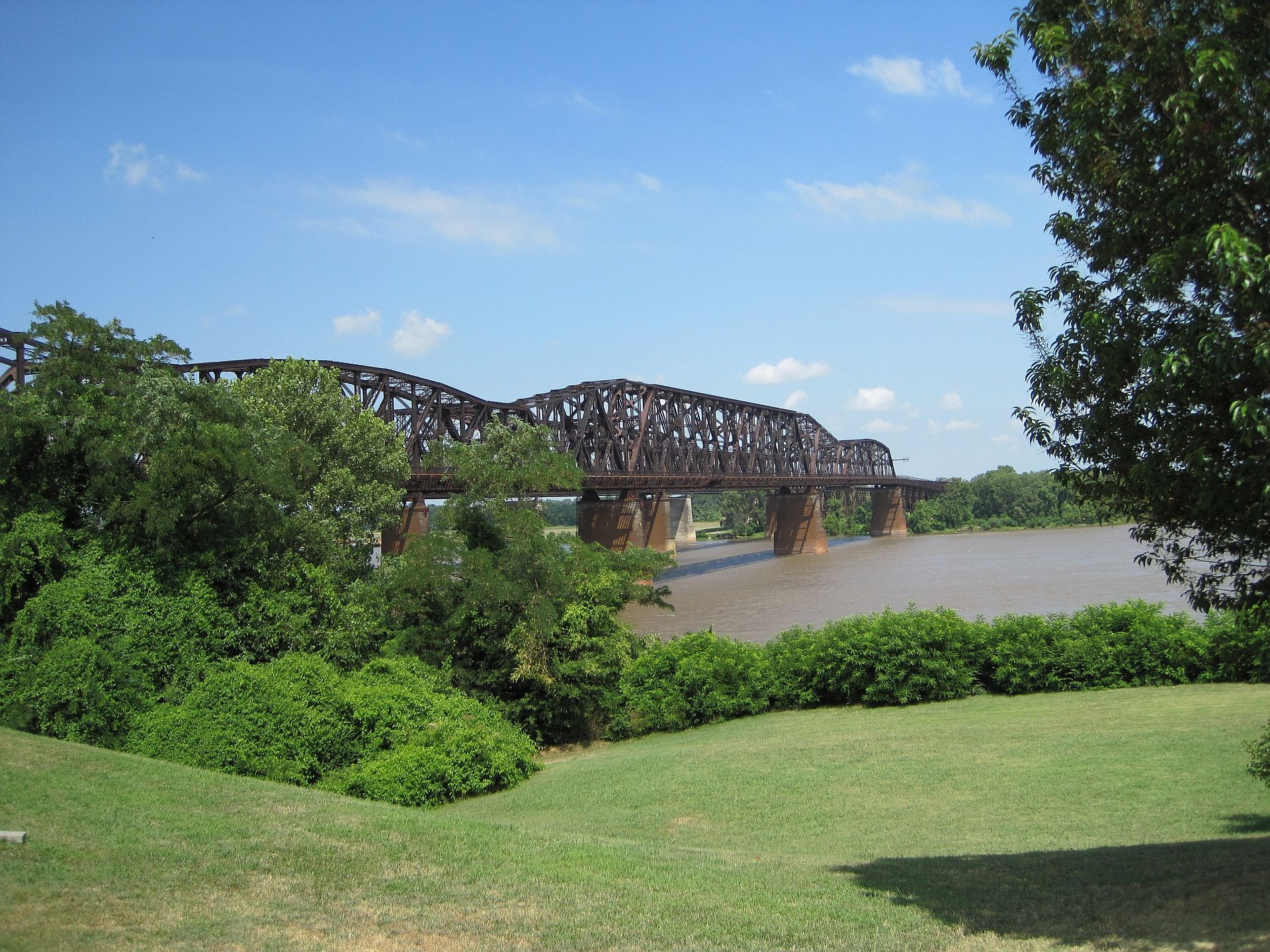 Large metal bridge over a wide river, surrounded by green trees and grass. - Memphis Riverwalk
