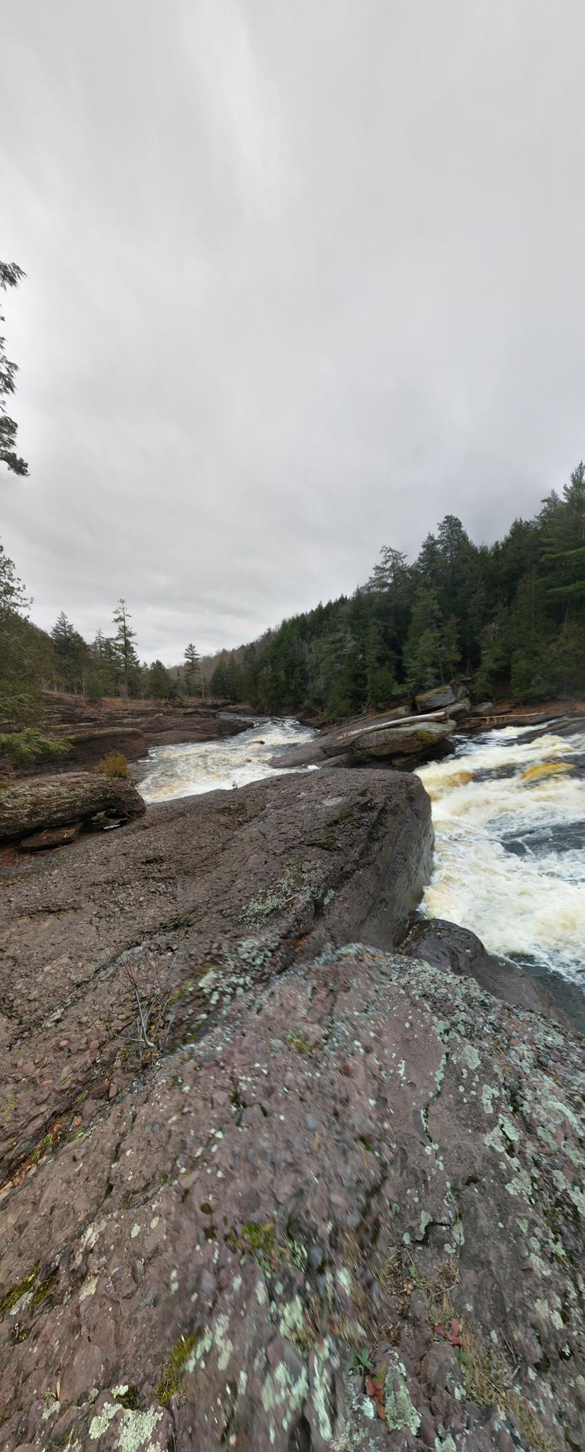 A wide river flows over dark rocks under an overcast sky.