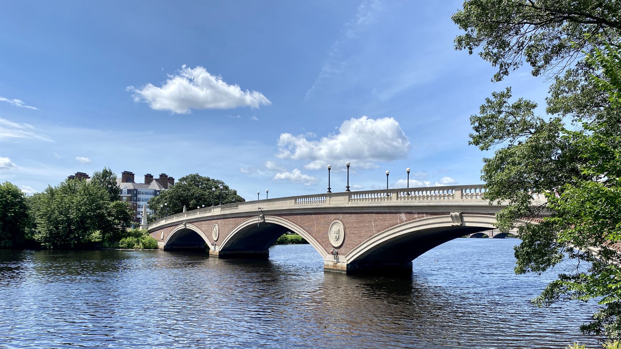 An arched bridge over a river, with trees and buildings under a blue sky. - Dr. Paul Dudley White Path Loop