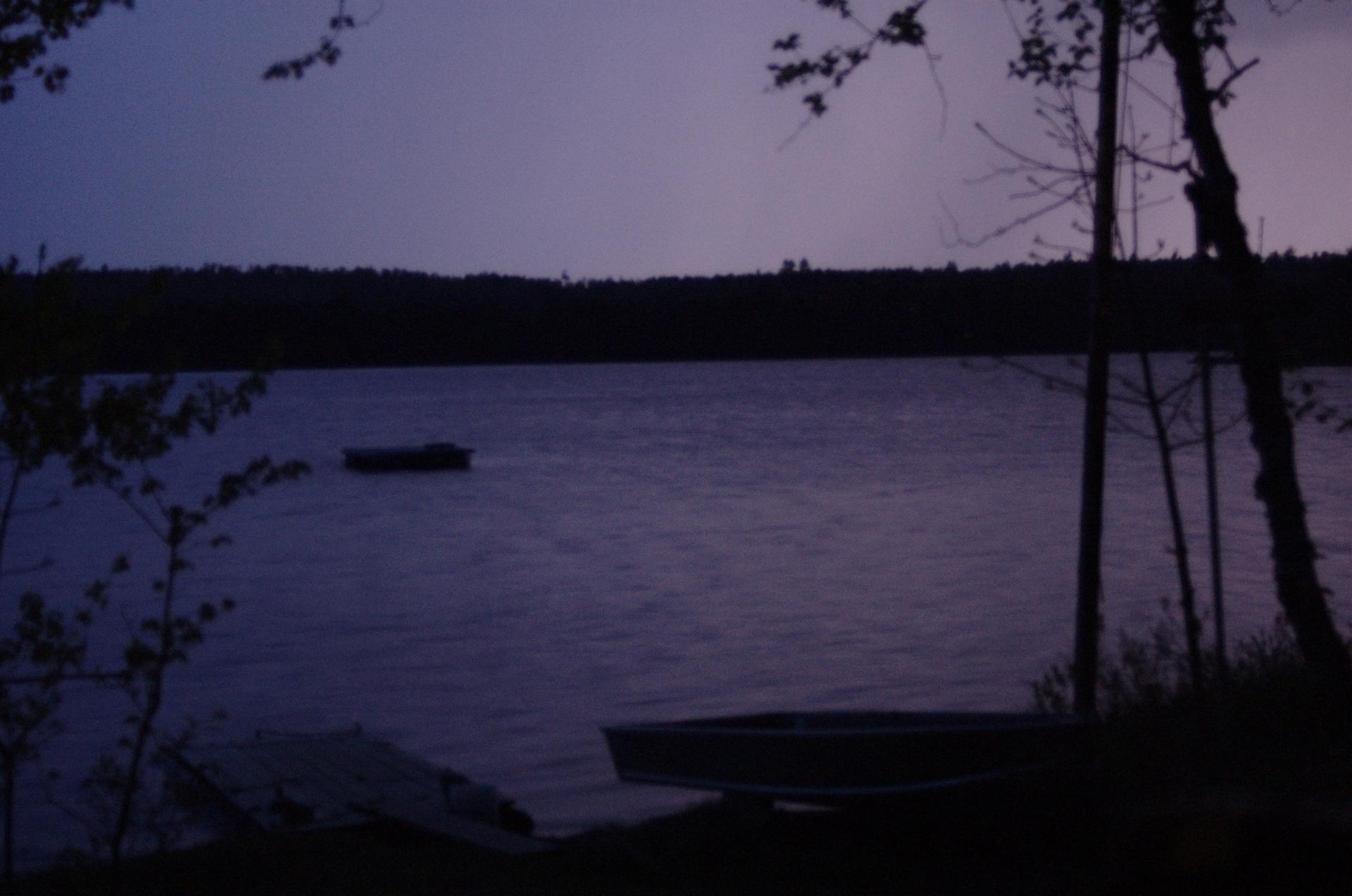 A dark lake at twilight with two boats and silhouetted trees.