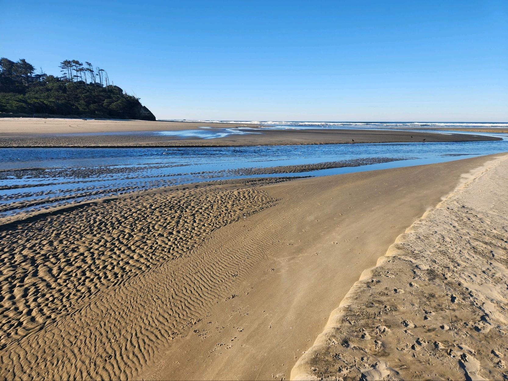 Sunny wide sandy beach with a tidal river flowing towards the ocean.
