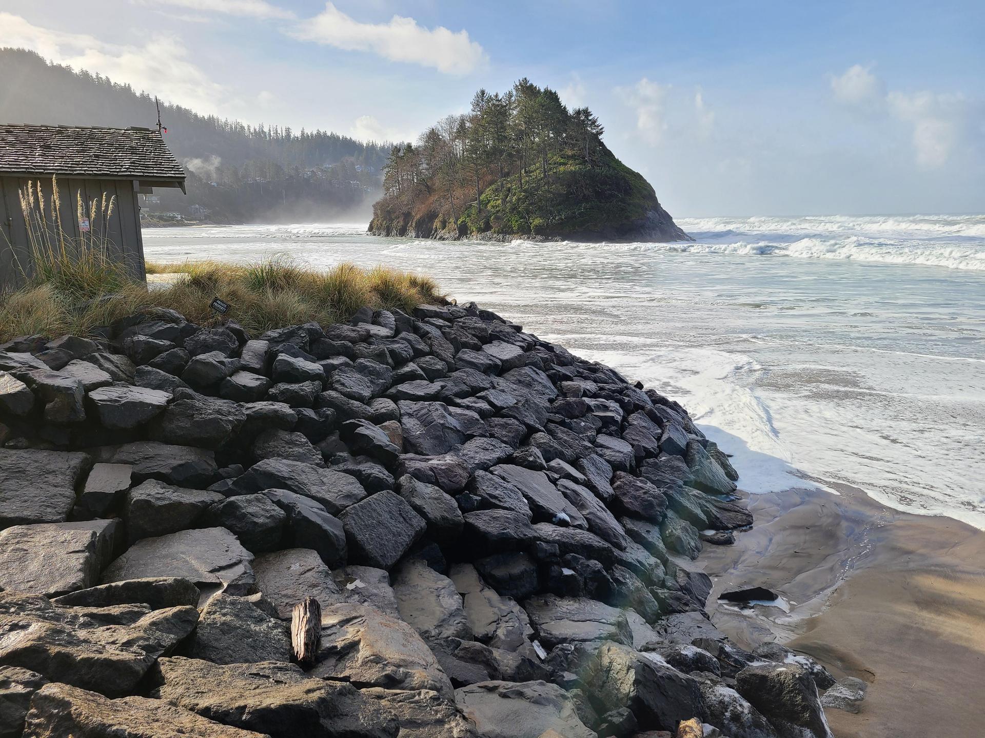 Rocky seawall protecting a sandy beach from ocean waves, with a distant island.