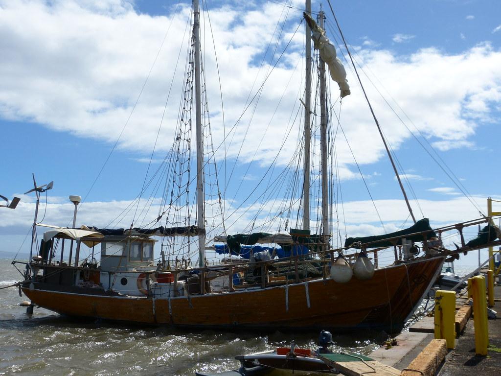 A large wooden schooner docked by a pier under a bright, cloudy sky.