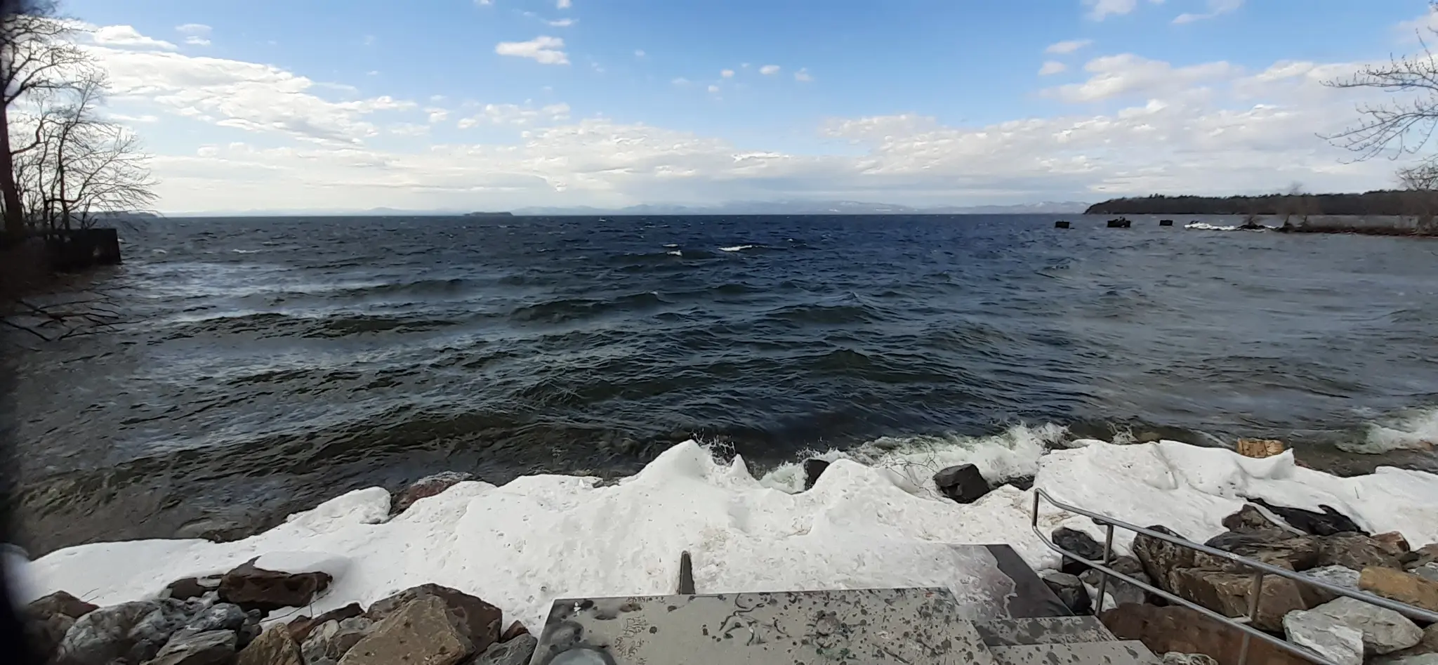 Choppy dark water crashes against an icy, rocky shore under a cloudy sky.