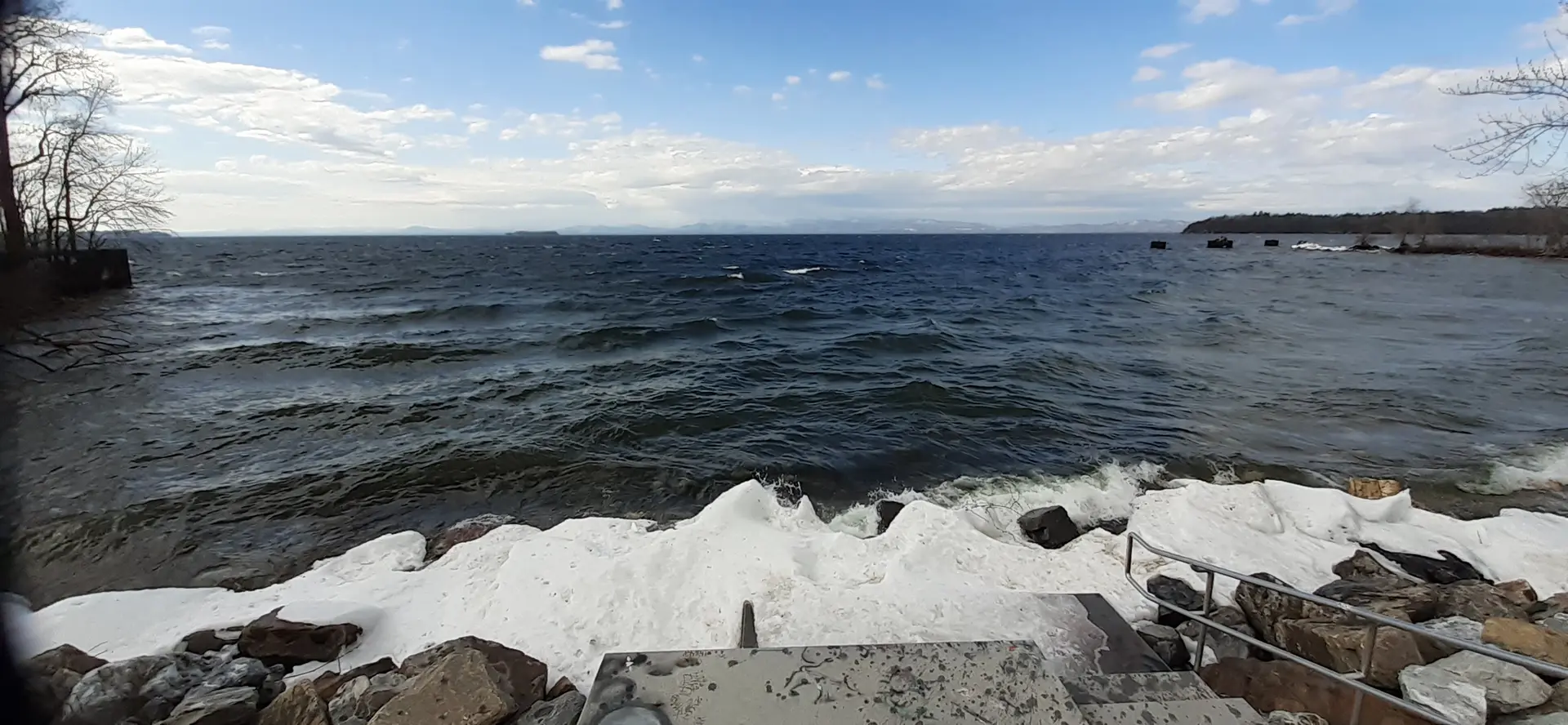 Choppy dark water crashes against an icy, rocky shore under a cloudy sky.