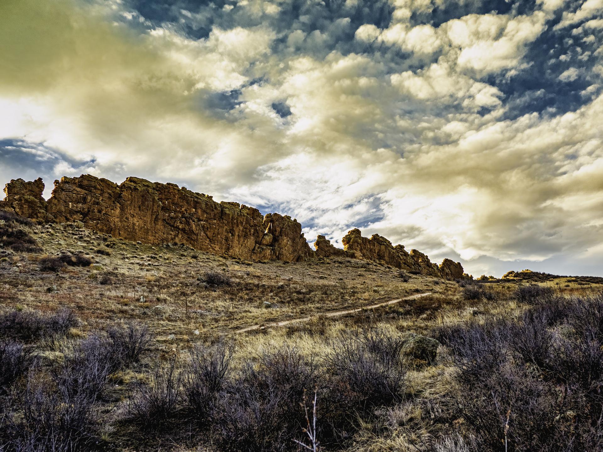 Dramatic landscape with large rock formations on a hill under a cloudy sky.