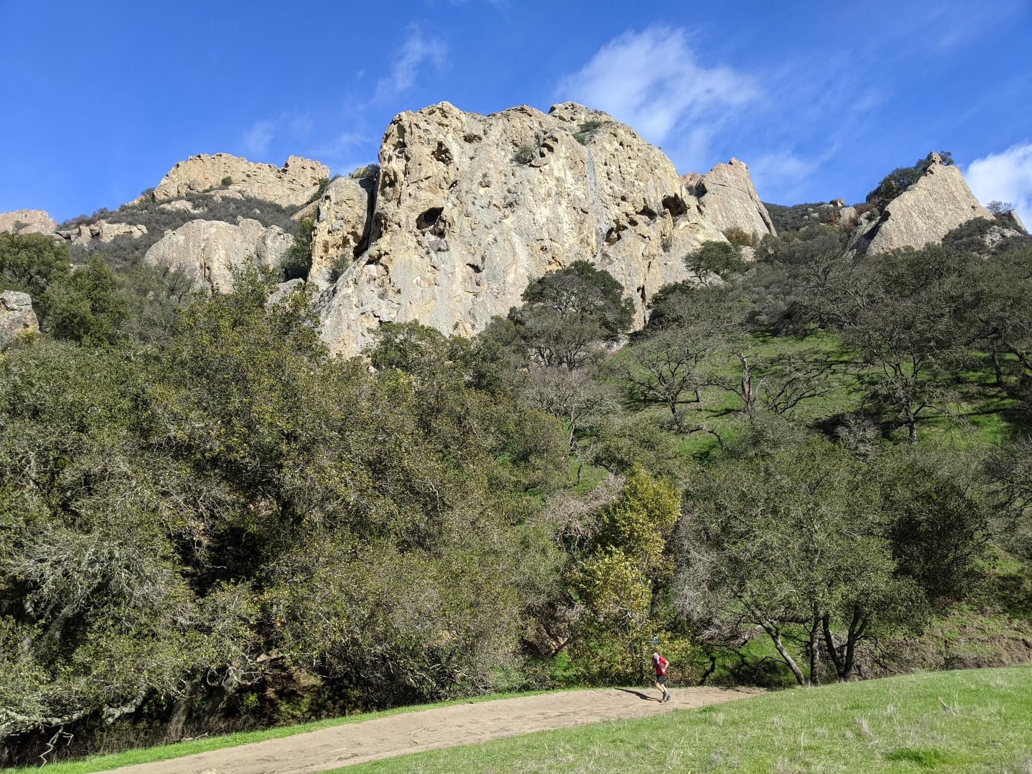 Large rocky mountain peak above a dirt path with a person walking. - Stage Road Trail