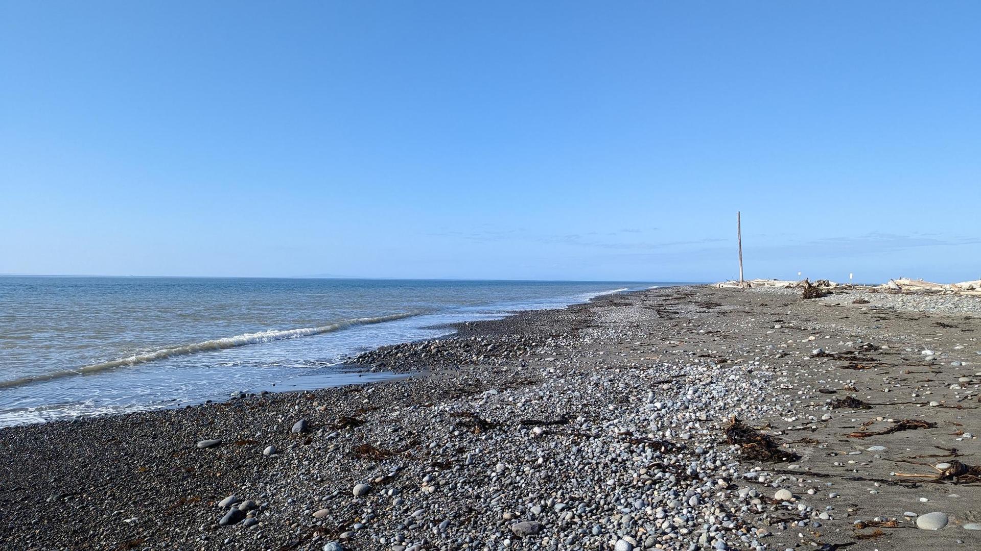 A wide, rocky beach with gentle waves under a clear blue sky.