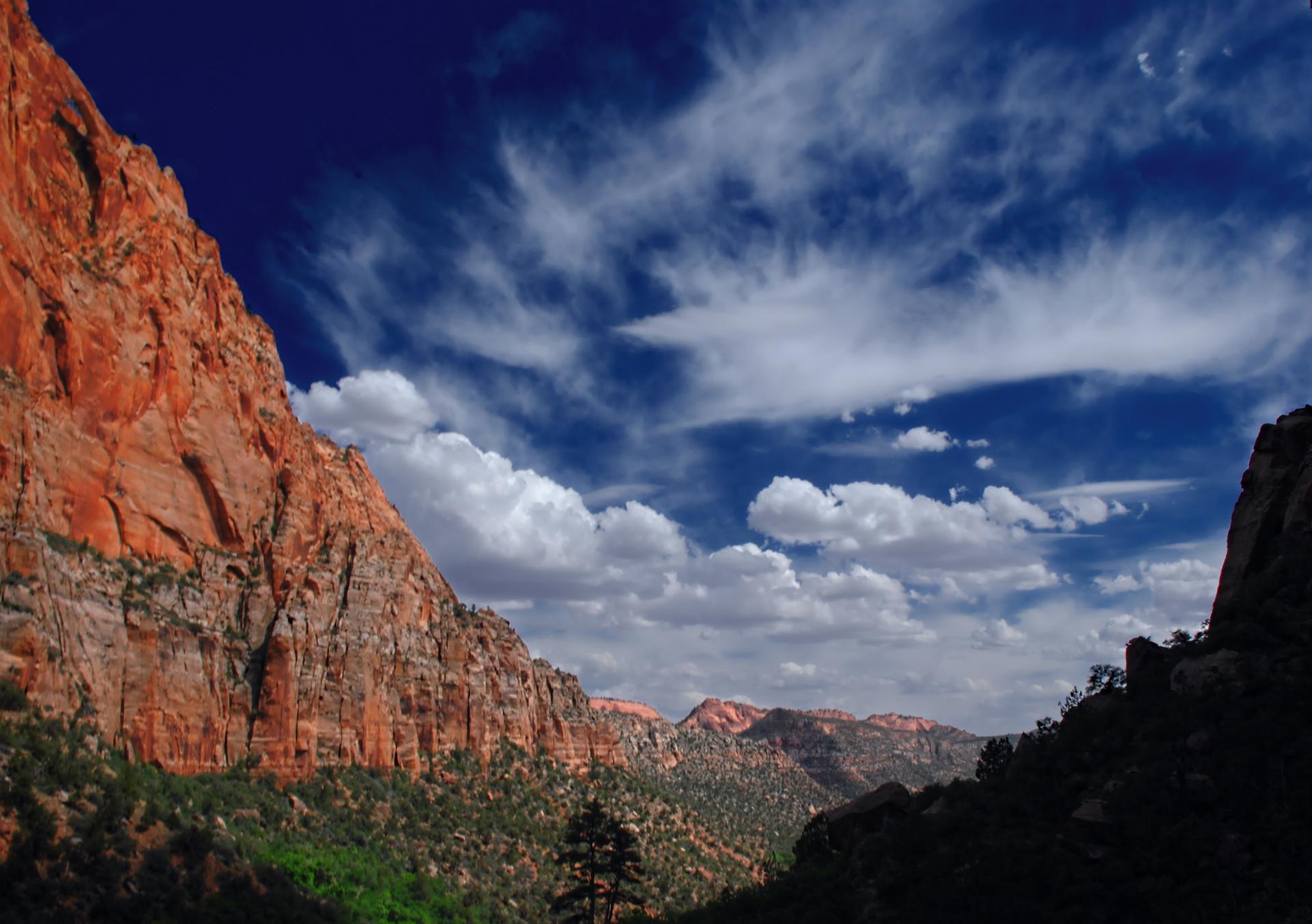 Vast red rock canyon under a dramatic blue sky with white clouds.