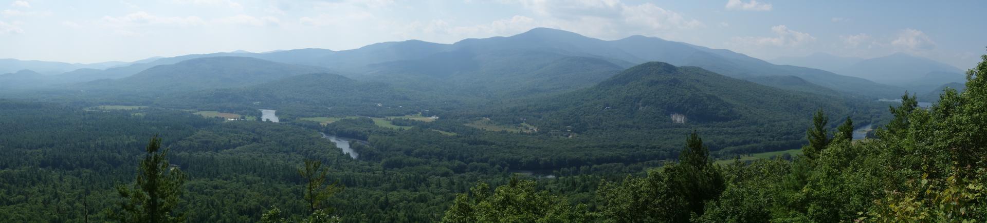 Panoramic view of a vast forested valley with a winding river and hazy distant mountains.