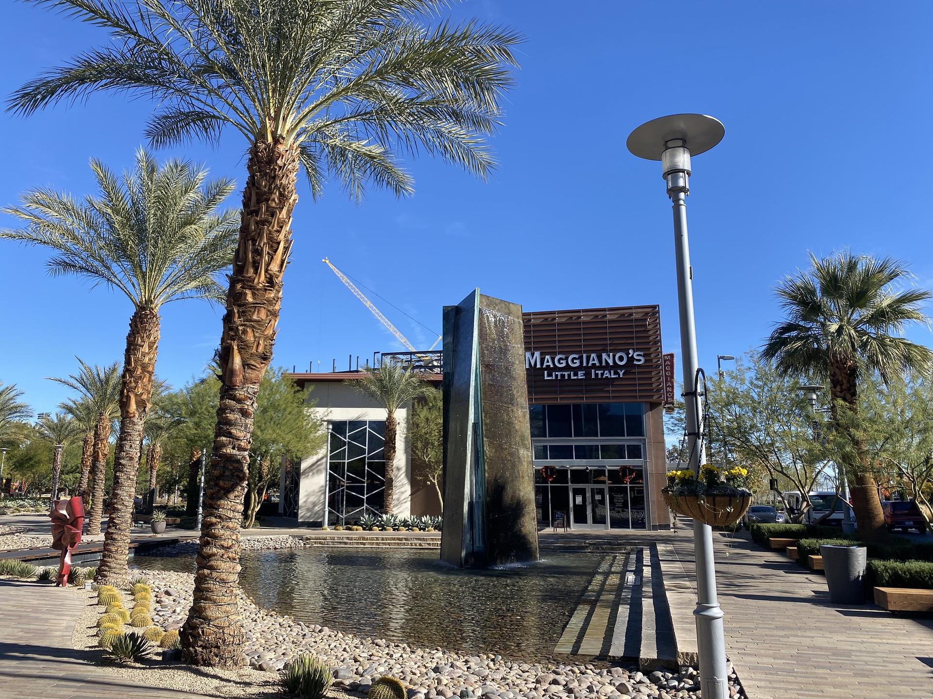 A fountain and palm trees in front of a restaurant under a clear sky.