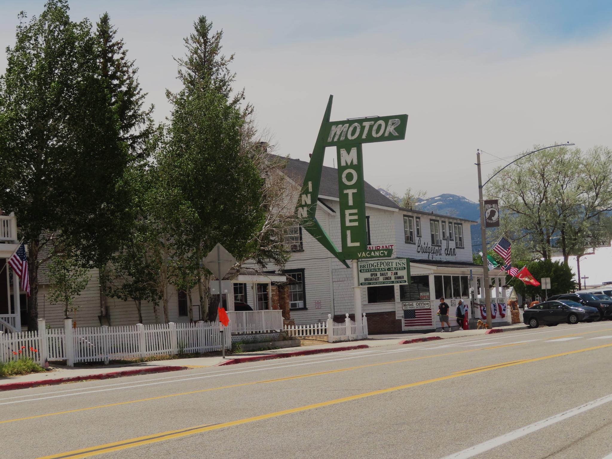 White motel building with a green sign on a street with cars and people.