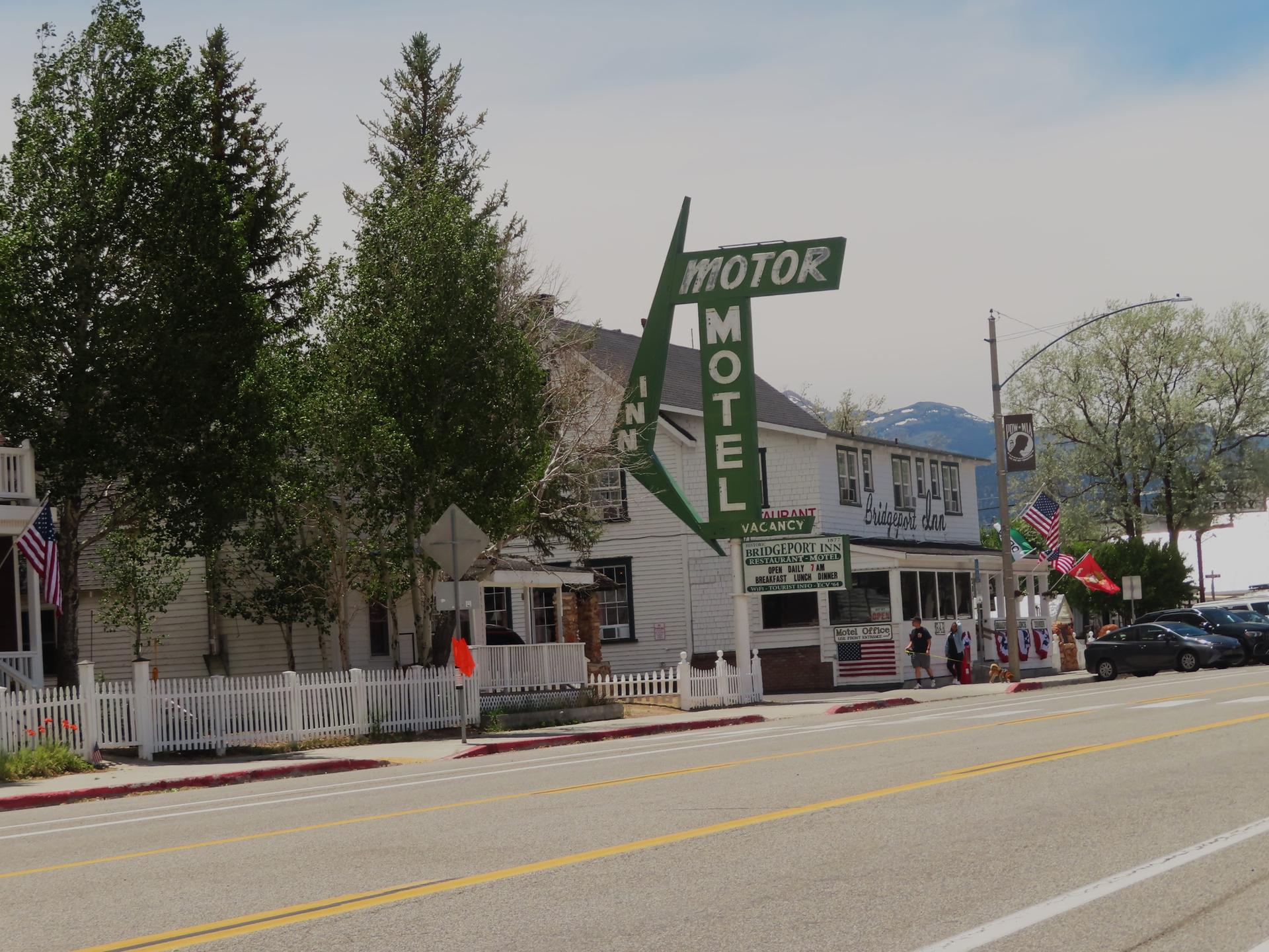 White motel building with a green sign on a street with cars and people.