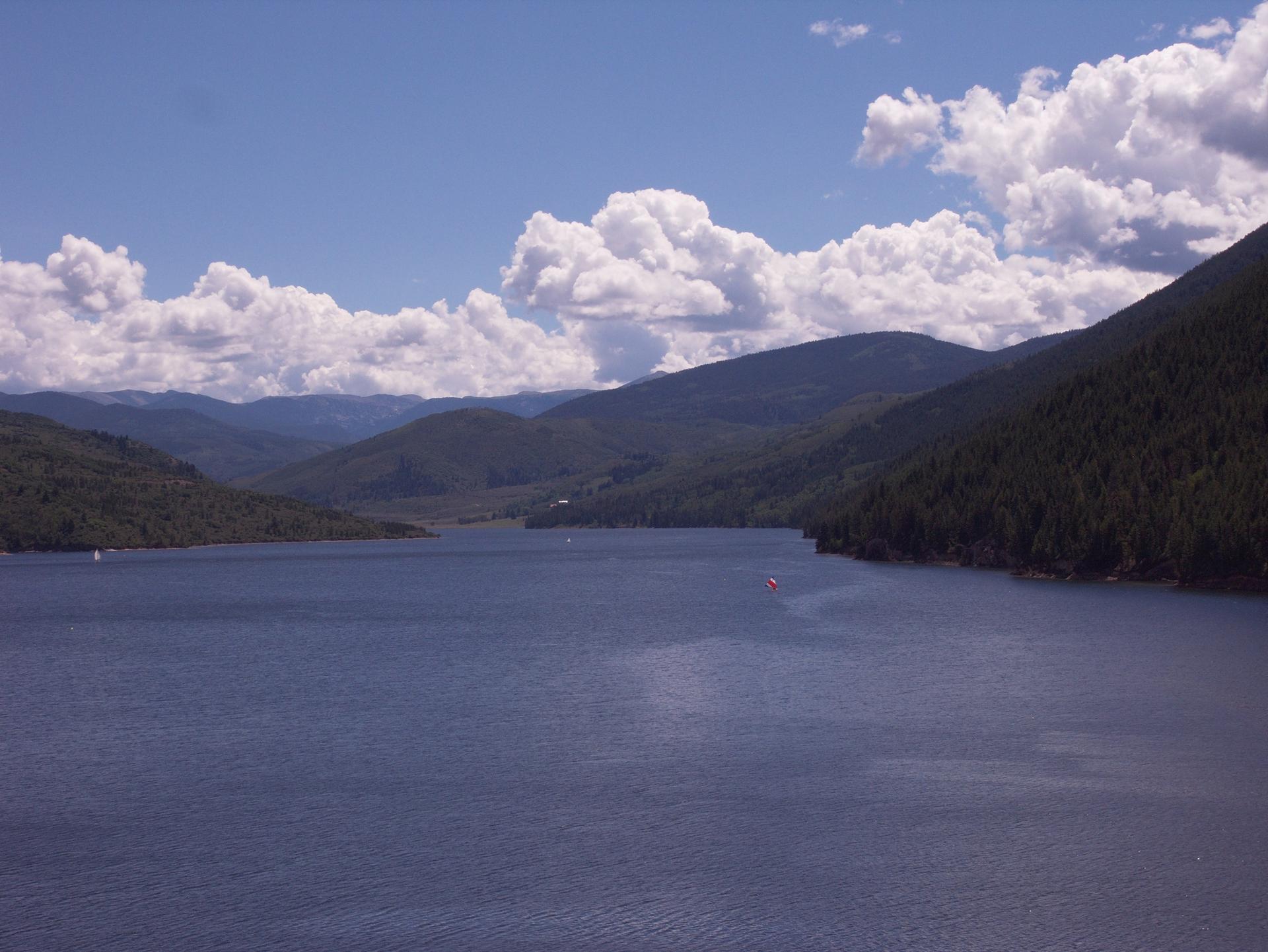 Vast blue lake surrounded by forested mountains under a partly cloudy sky with small boats.