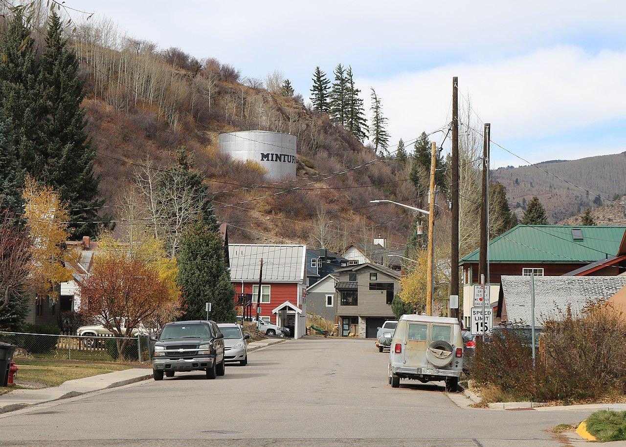 A quiet town street with houses and a water tank on a hillside.