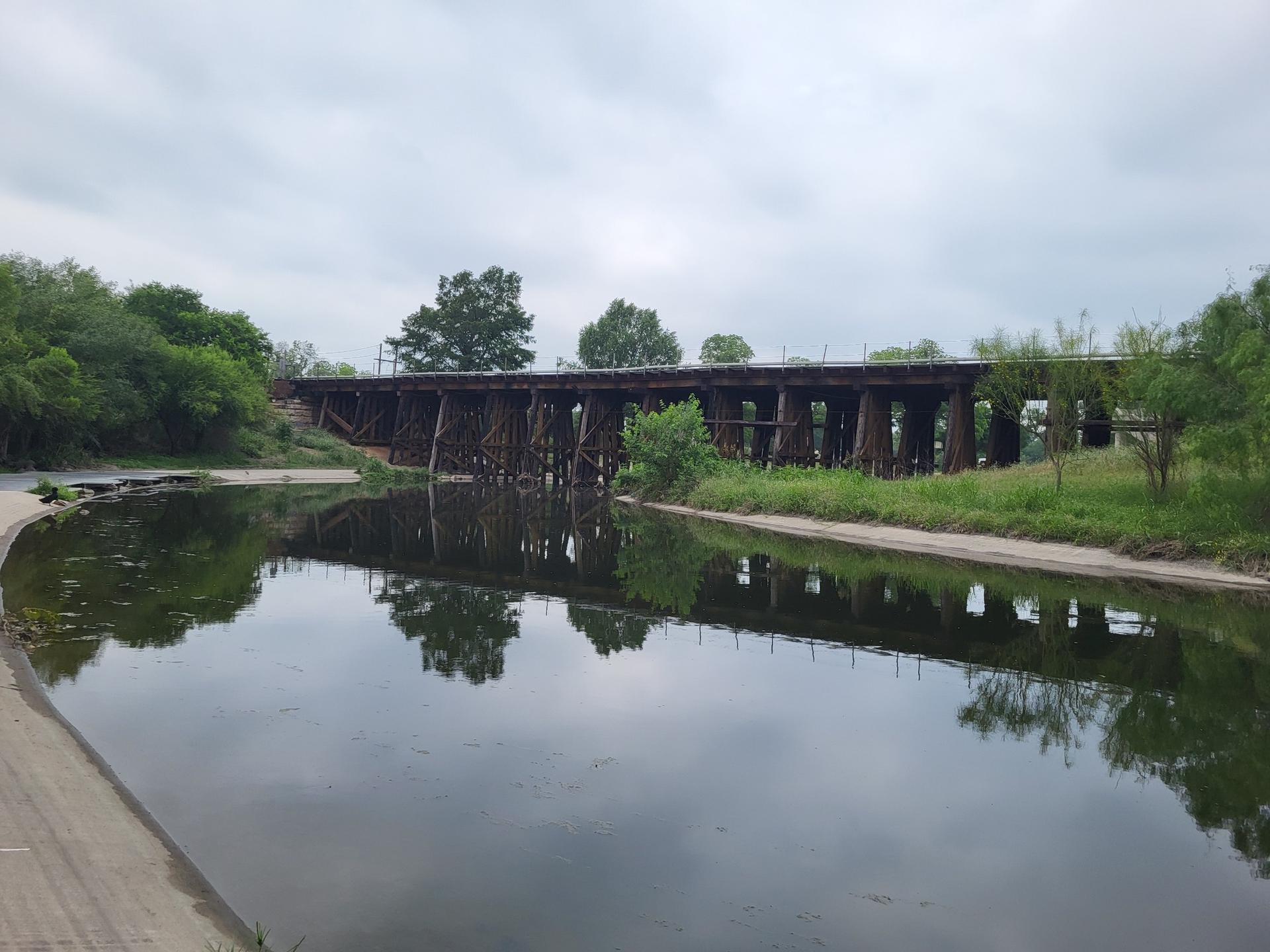 Wooden bridge spanning a calm river under an overcast sky.
