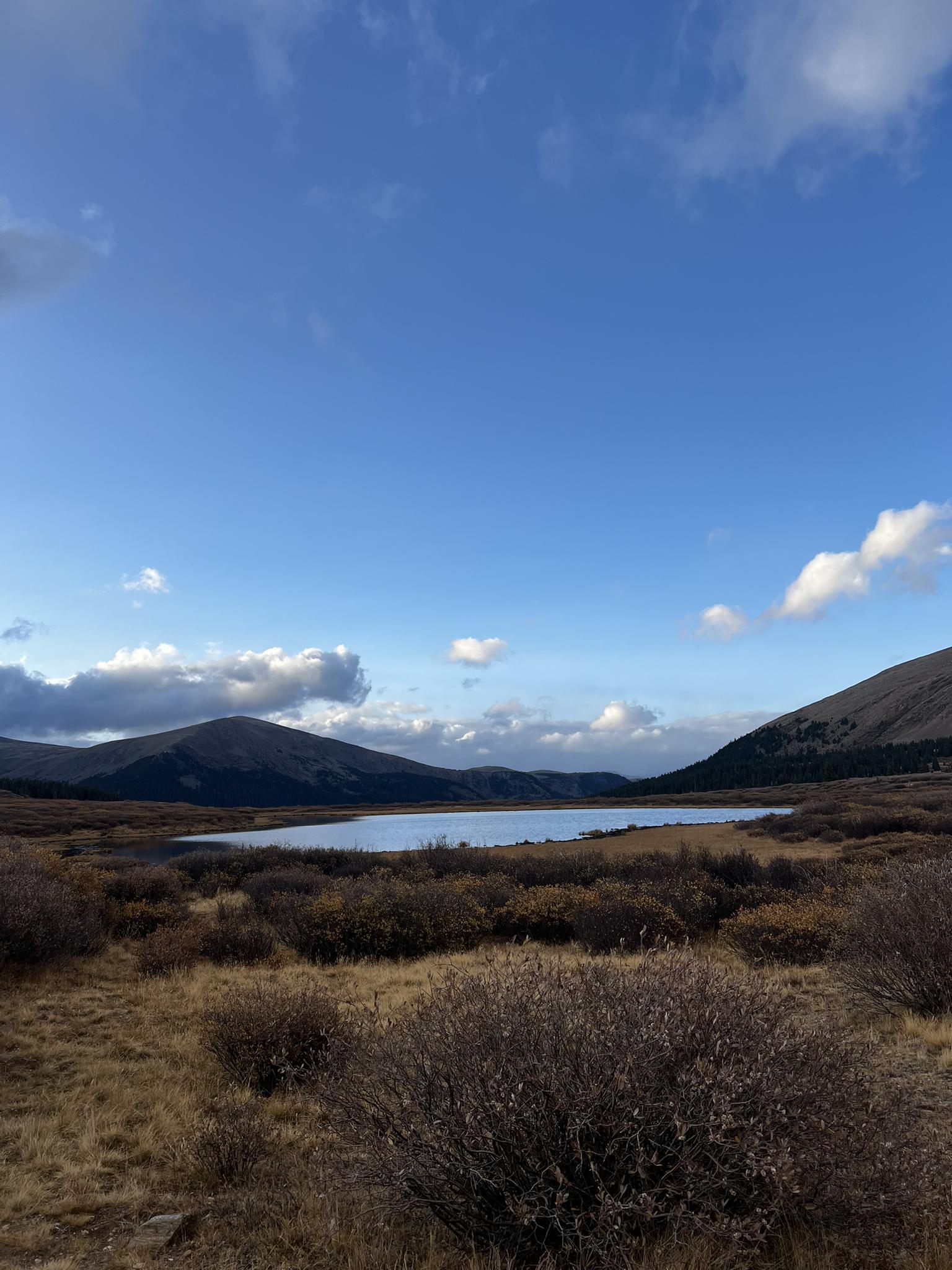 A serene mountain lake surrounded by dry brush under a partly cloudy sky.