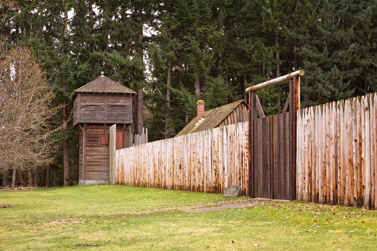 Wooden fort with watchtower and palisade fence, surrounded by trees.