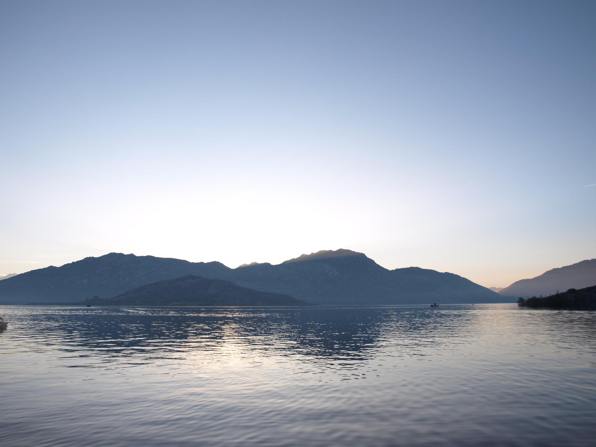Calm lake reflecting distant mountains under a soft, clear sky.