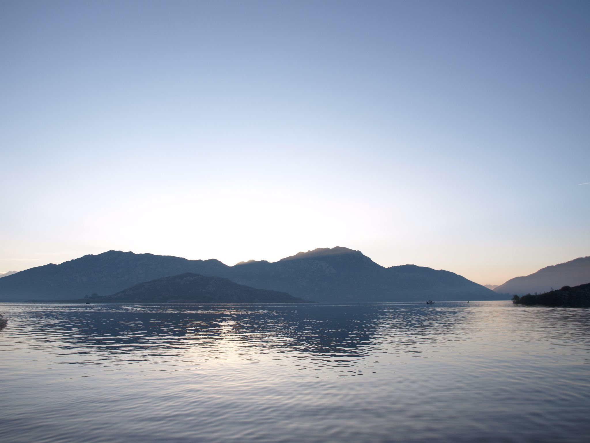 Calm lake reflecting distant mountains under a soft, clear sky. - Lake Perris – Scenic Cycling Spot loop from Lake Perris