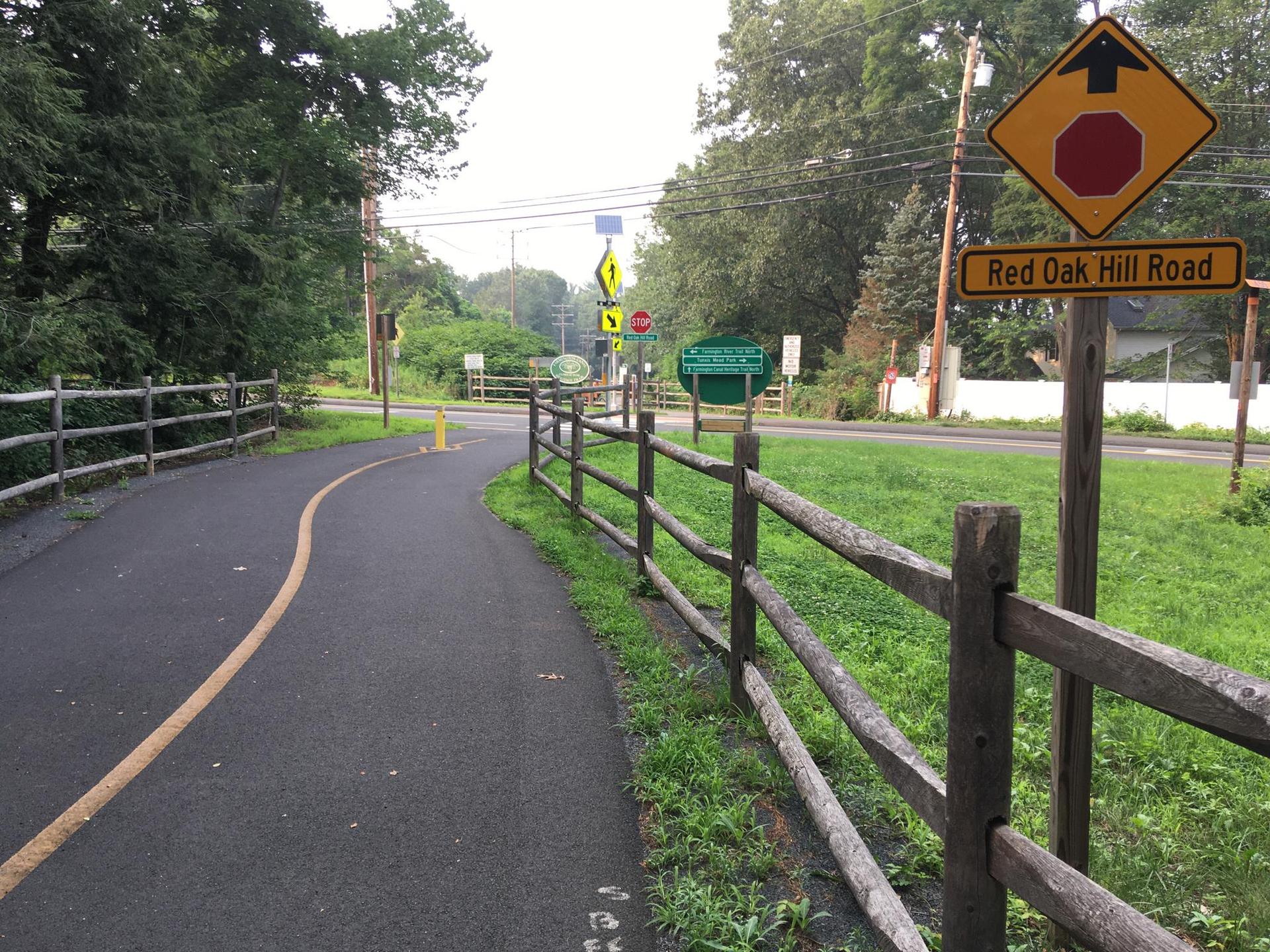Paved path with a yellow line, wooden fence, and road signs on an overcast day.