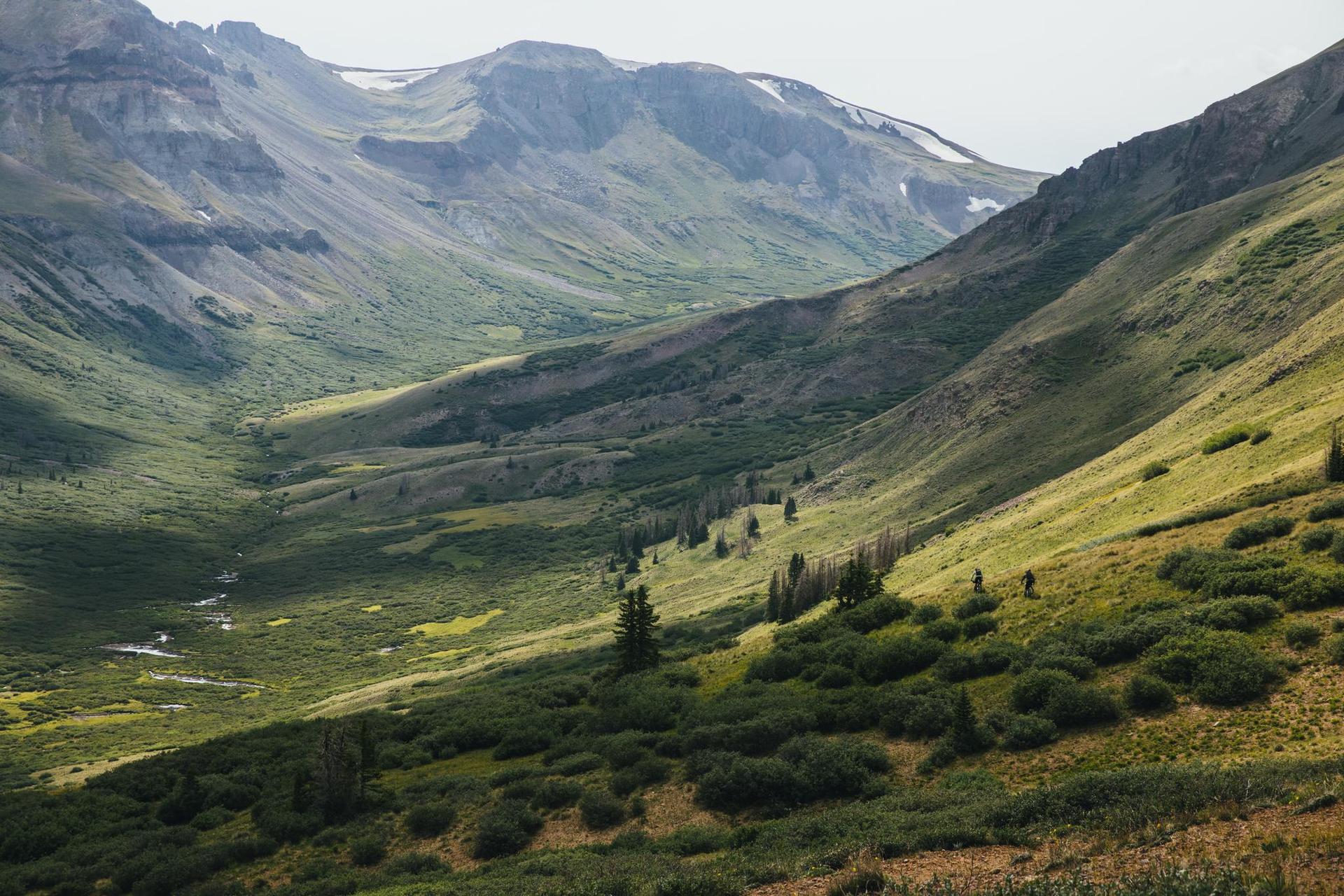 Lush green mountain valley with a winding stream and distant peaks.