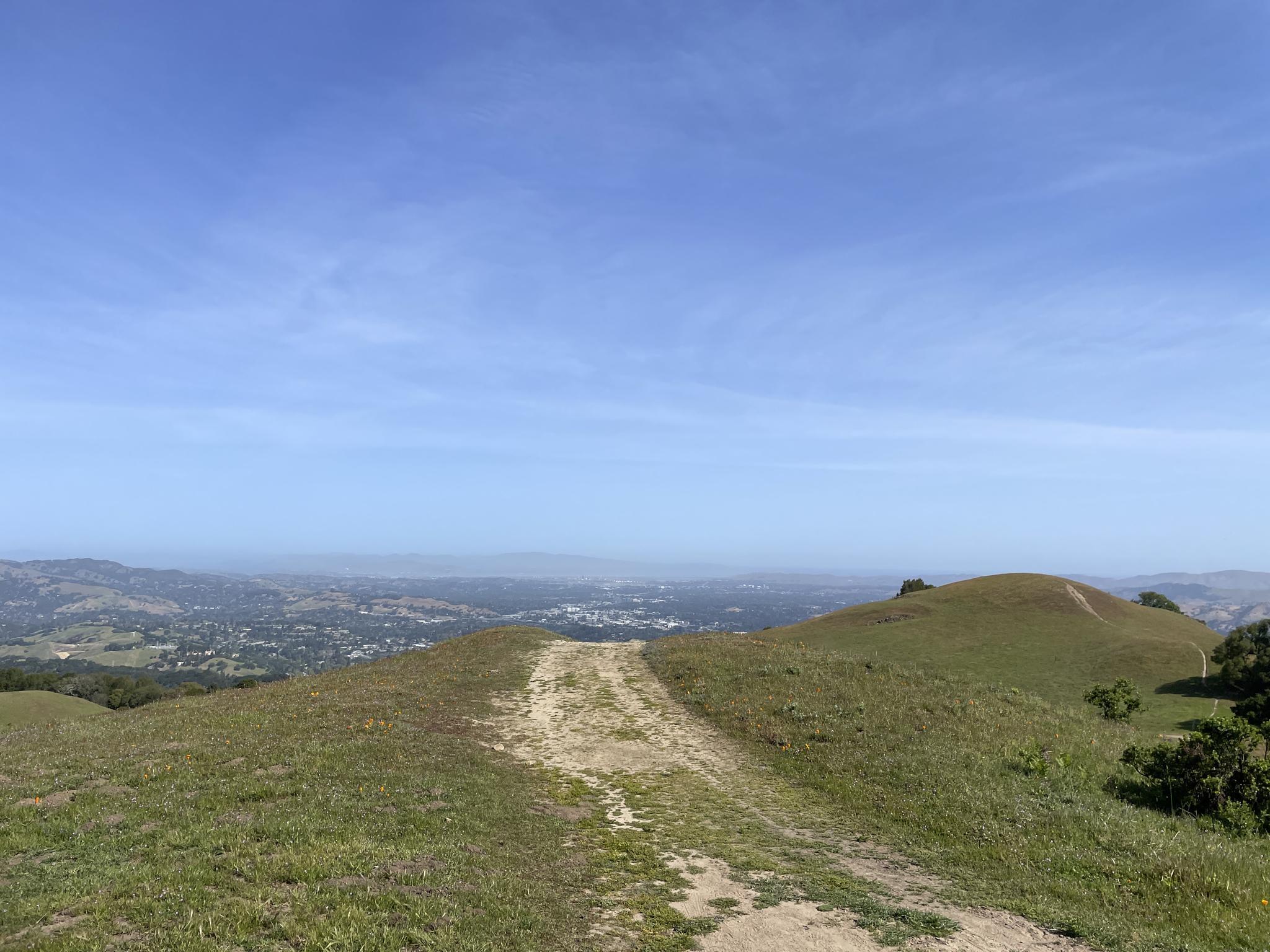 Dirt path on a grassy hill overlooking a distant town in a valley.