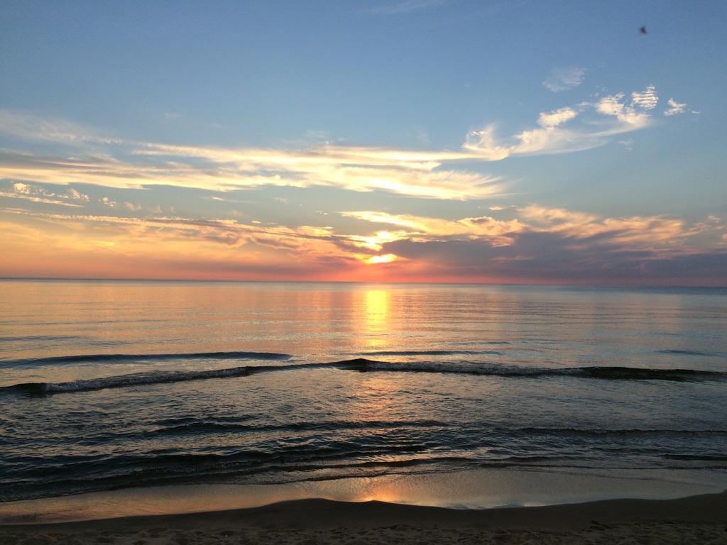 Vibrant sunset over calm water with a sandy beach in the foreground.