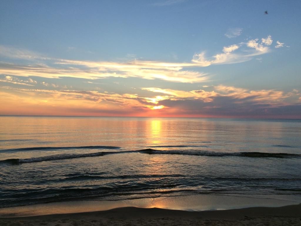 Vibrant sunset over calm water with a sandy beach in the foreground. - Saugatuck Dunes Outer Loop