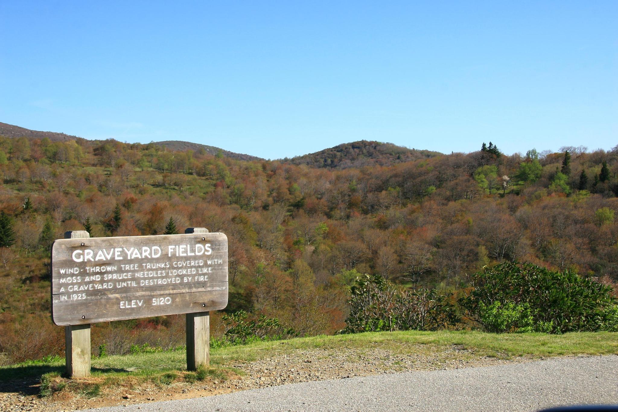 Wooden sign in a hilly landscape with autumn trees under a clear sky.